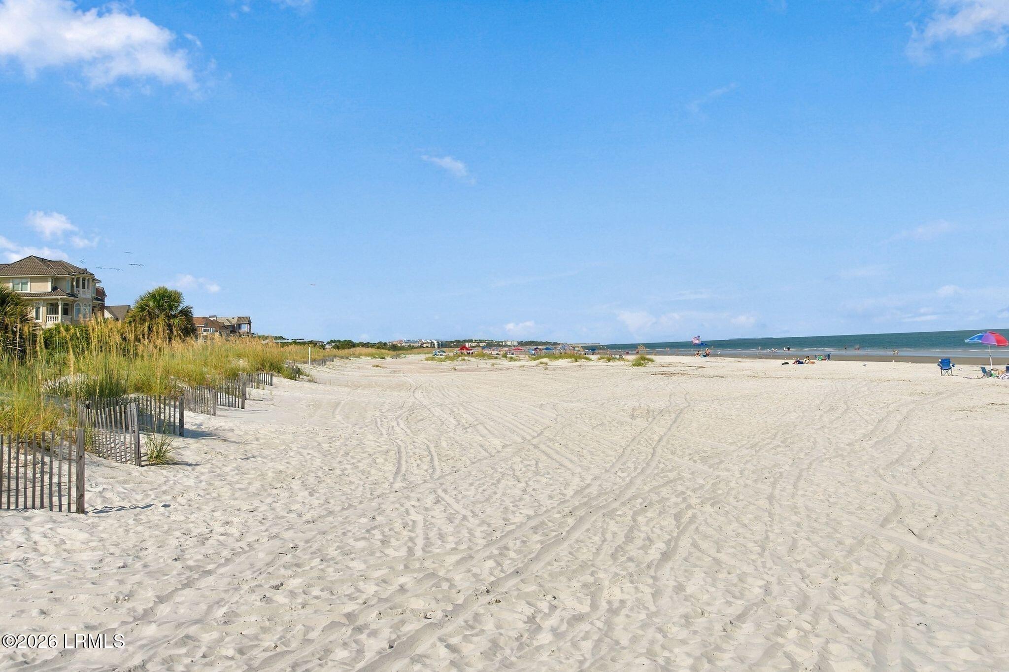 Sandy beach with dune grass, shoreline umbrellas, and houses along the coast.