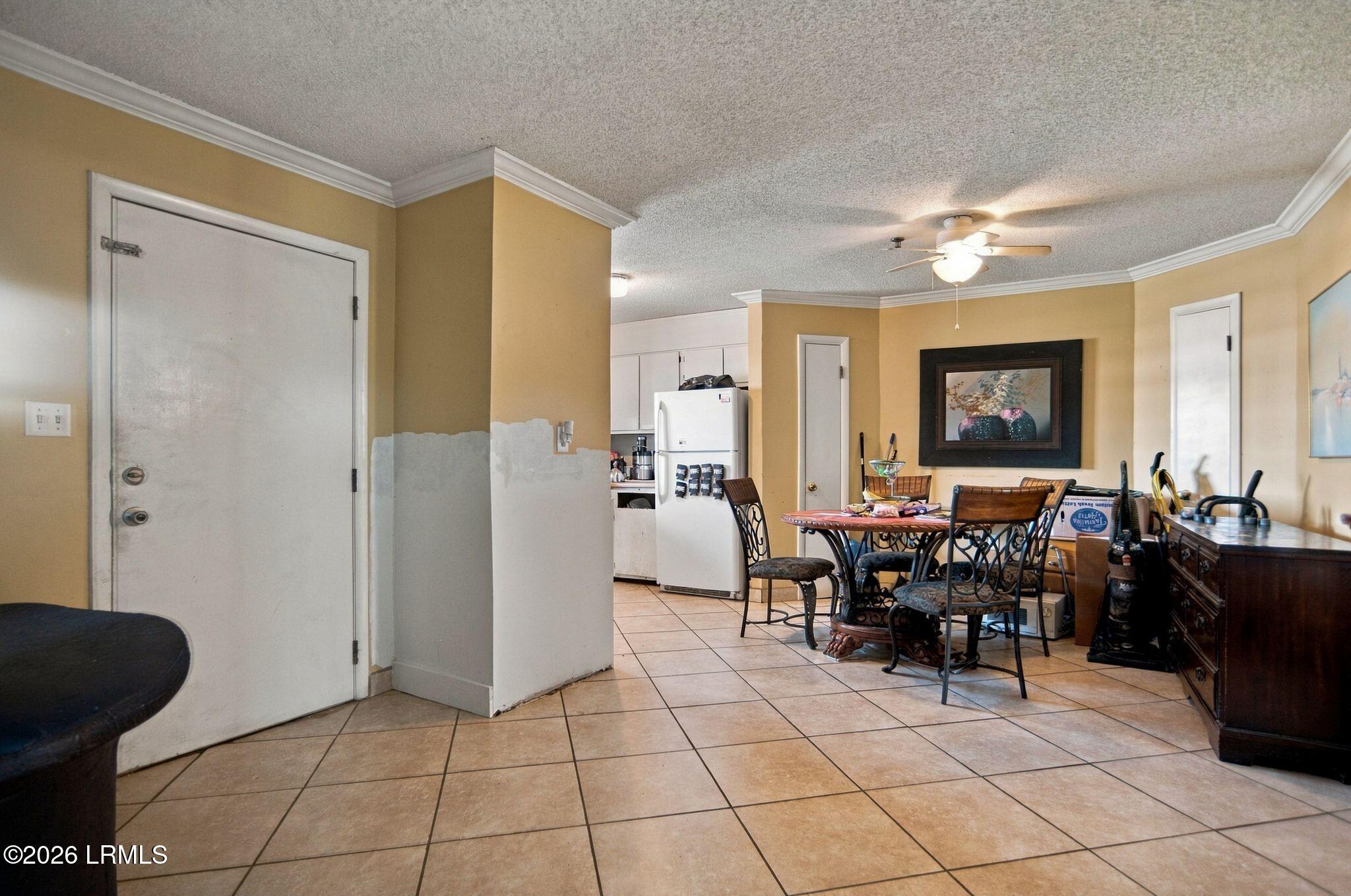 Dining area with tiled floors, a round table, dark wood sideboard, and kitchen beyond.