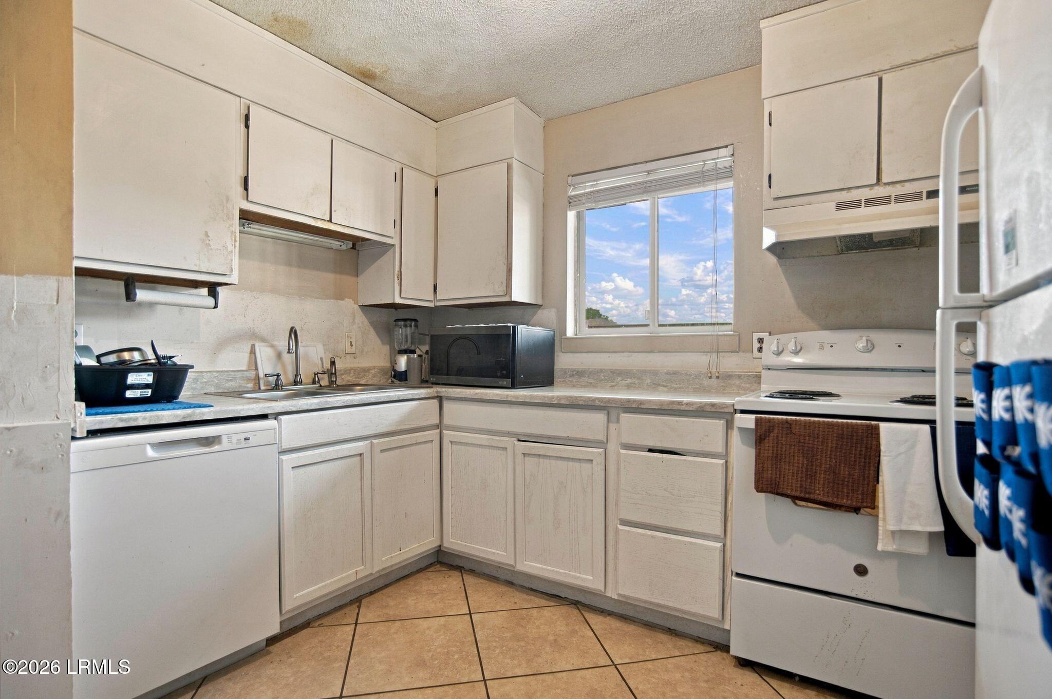 Kitchen with white cabinets, tan tile floor, and a window above the counter.