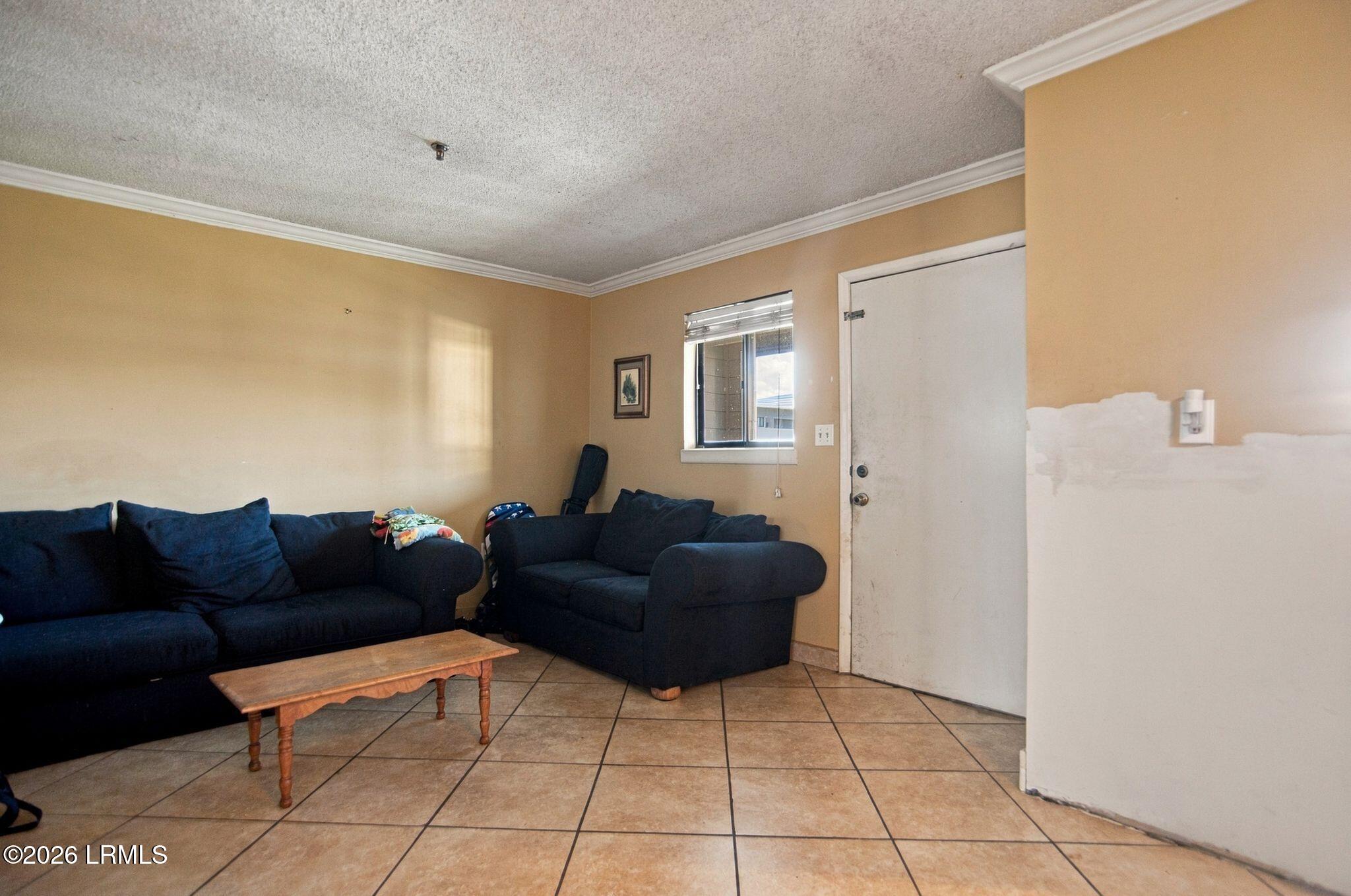 Living room with navy sofas, a wooden coffee table, tiled floor, and an unfinished wall patch.
