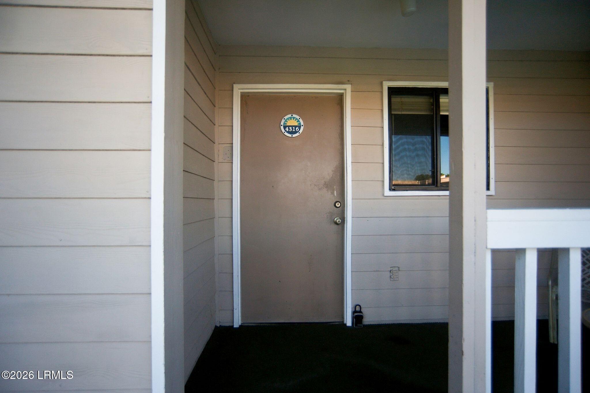 Covered entrance to unit 4316 with a brown door, circular number sign, and adjacent window.