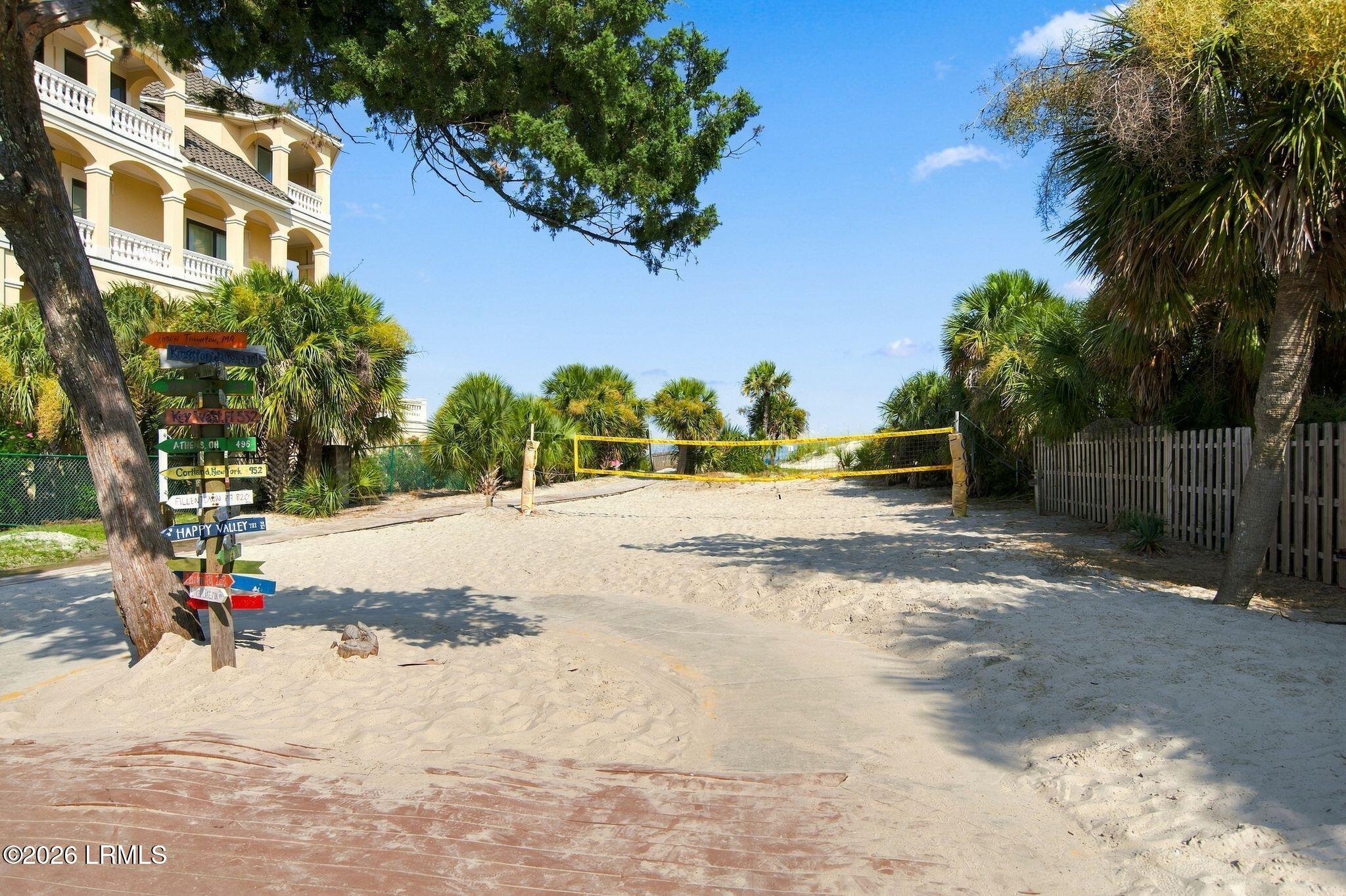 Sandy volleyball court beside a palm-lined condominium, with colorful directional signs.