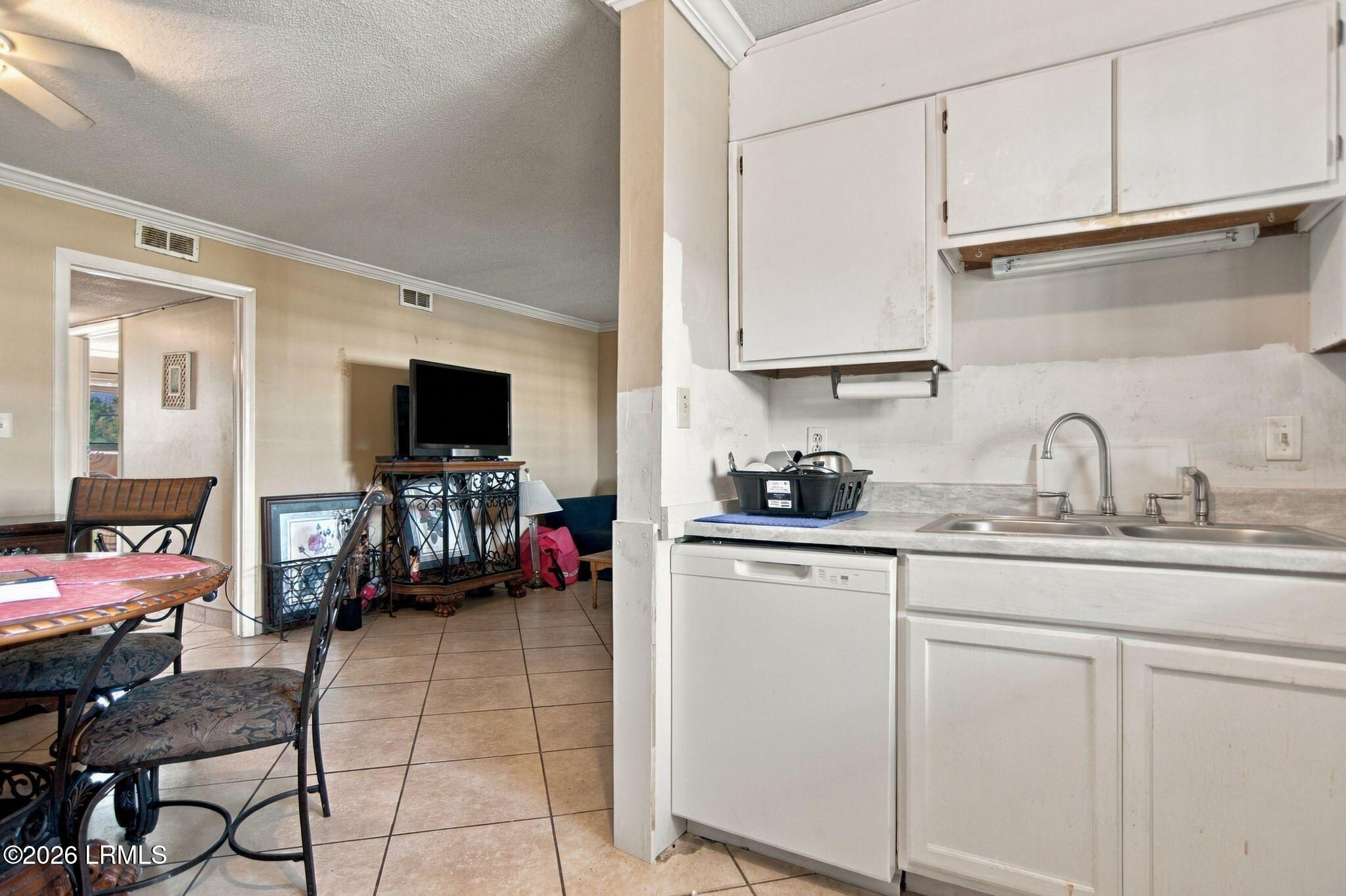 Kitchen with white cabinets and sink opening onto a tiled dining and living area.
