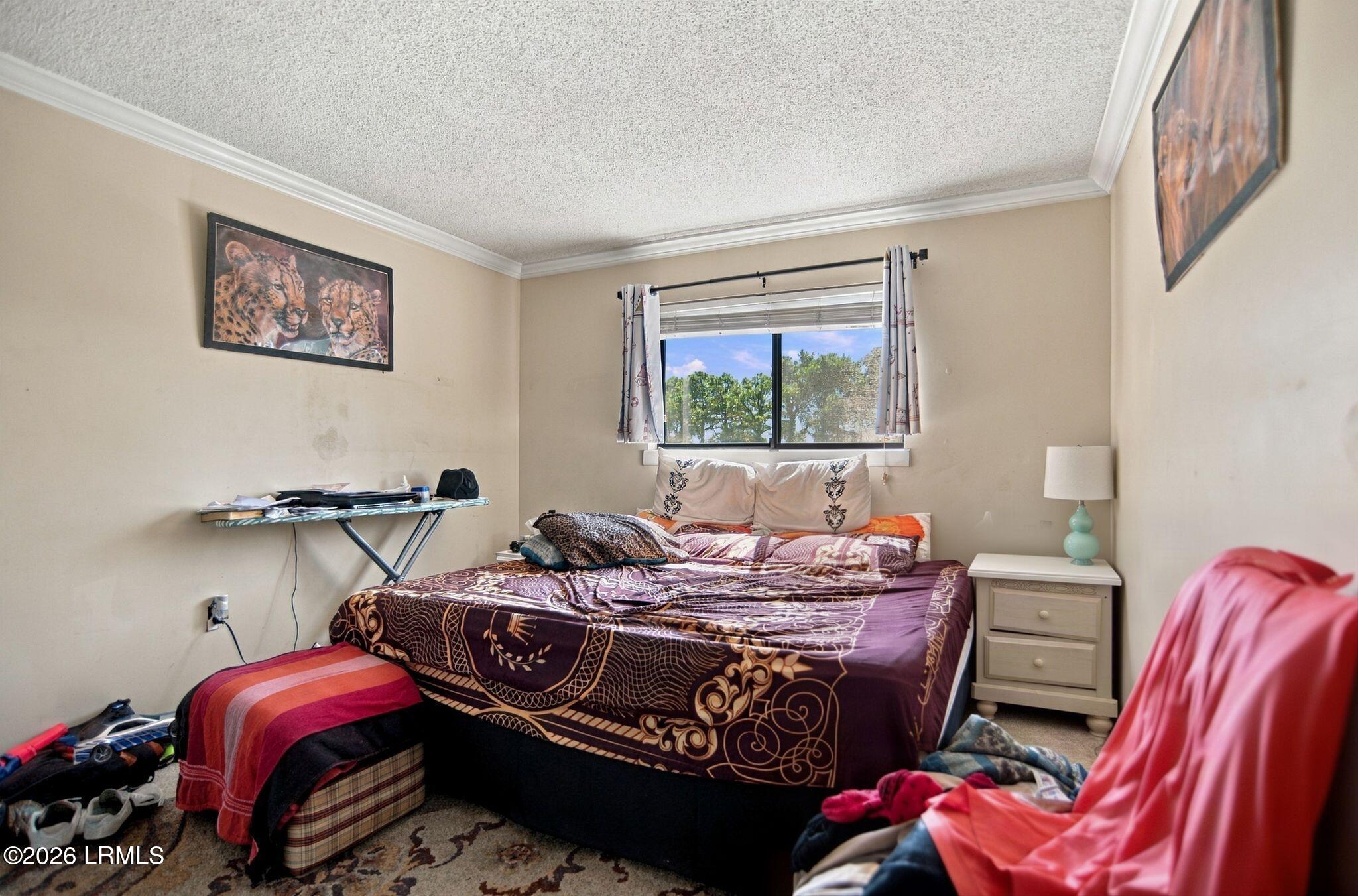 Bedroom with a patterned bedspread, curtained window, and personal items around the room.