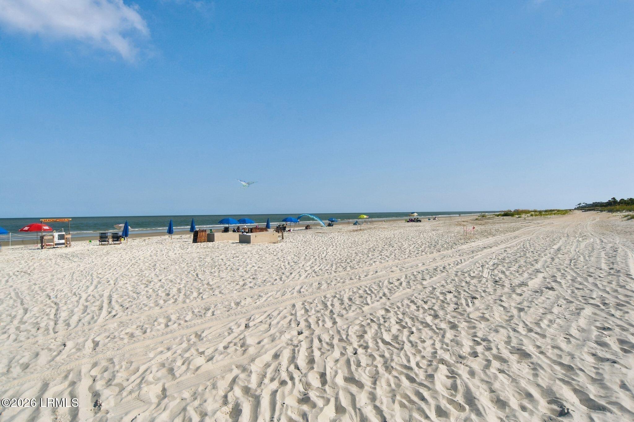 Wide sandy beach with tire tracks, colorful umbrellas, and ocean shoreline.
