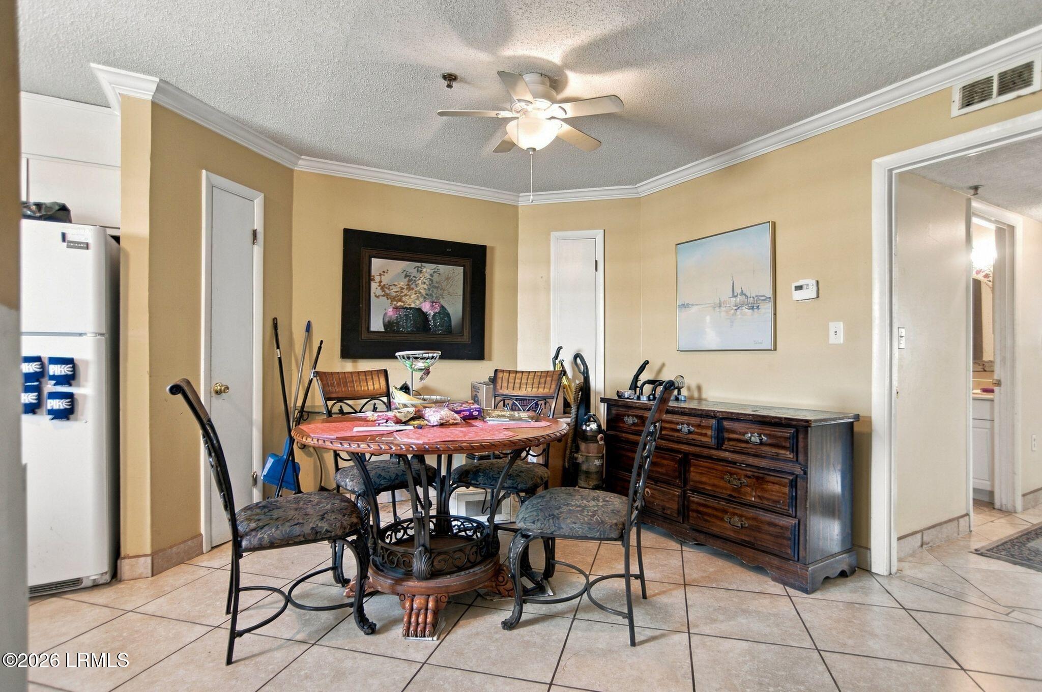 Dining area with a round wooden table, tiled floor, ceiling fan, and dark wood sideboard.