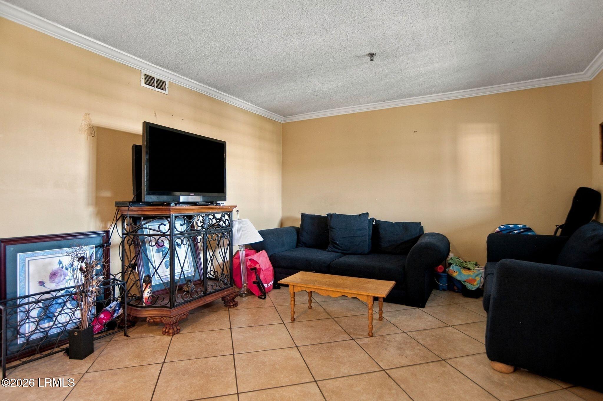 Living room with dark sofas, tiled floor, and a television on an ornate stand.