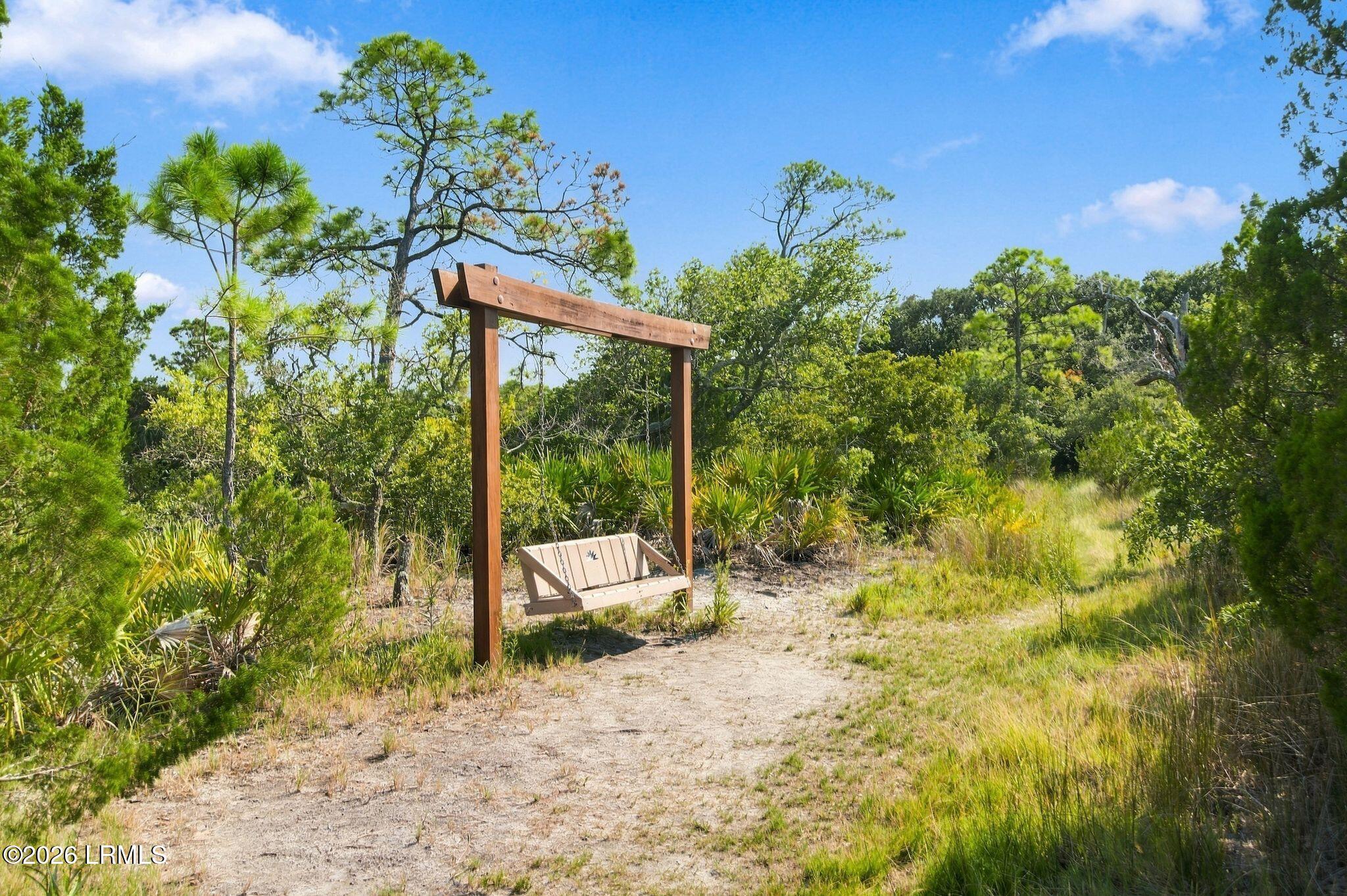 Hanging bench beside a sandy path amid coastal grasses and trees.