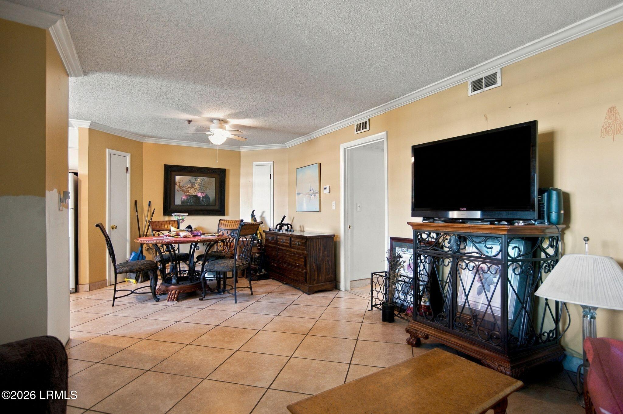 Furnished living and dining area with tiled floors, a large television, and ornate dark wood furniture.
