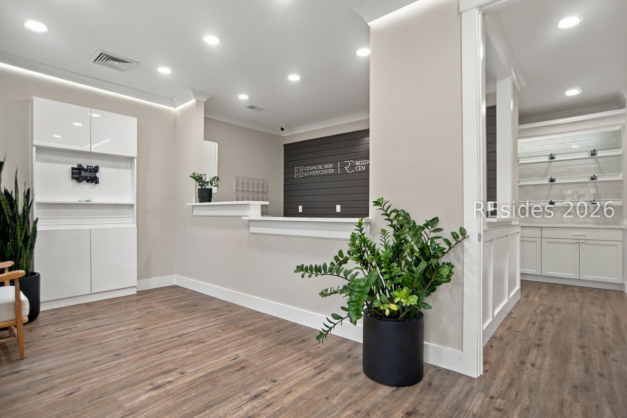 Cosmetic clinic reception with a white counter, dark slatted sign wall, and potted plants.