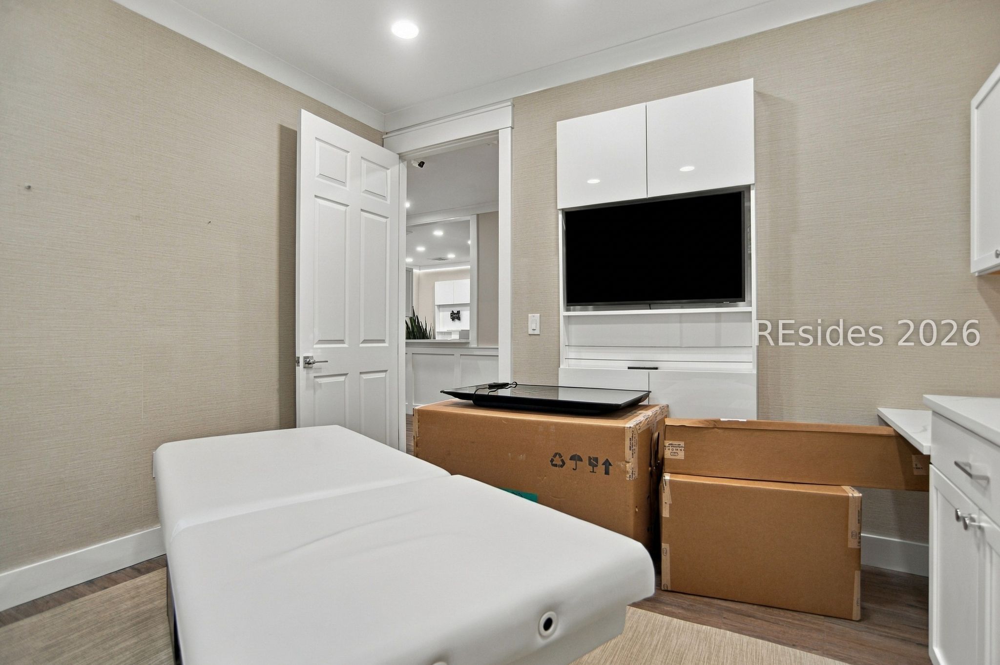 Treatment room with a white padded table, built-in television cabinetry, and unpacked boxes.