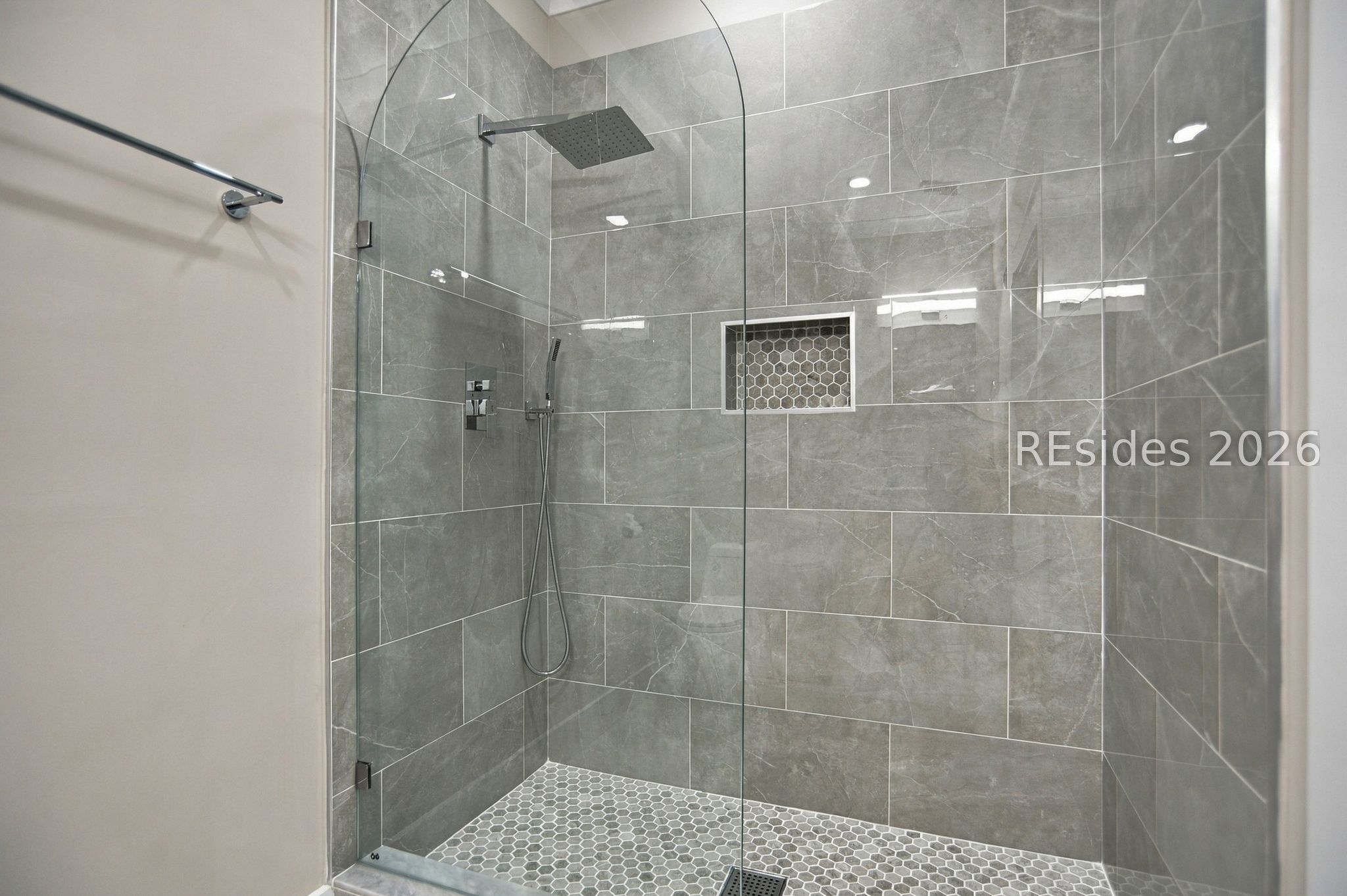 Walk-in shower with gray tile walls, hexagonal floor tiles, glass enclosure, and rainfall showerhead.