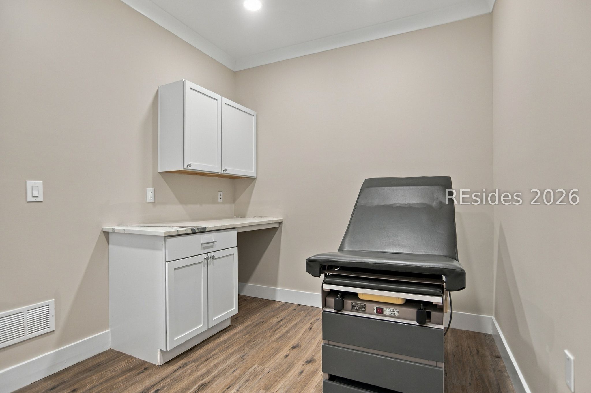 Clinical treatment room with an adjustable examination chair and white cabinetry.