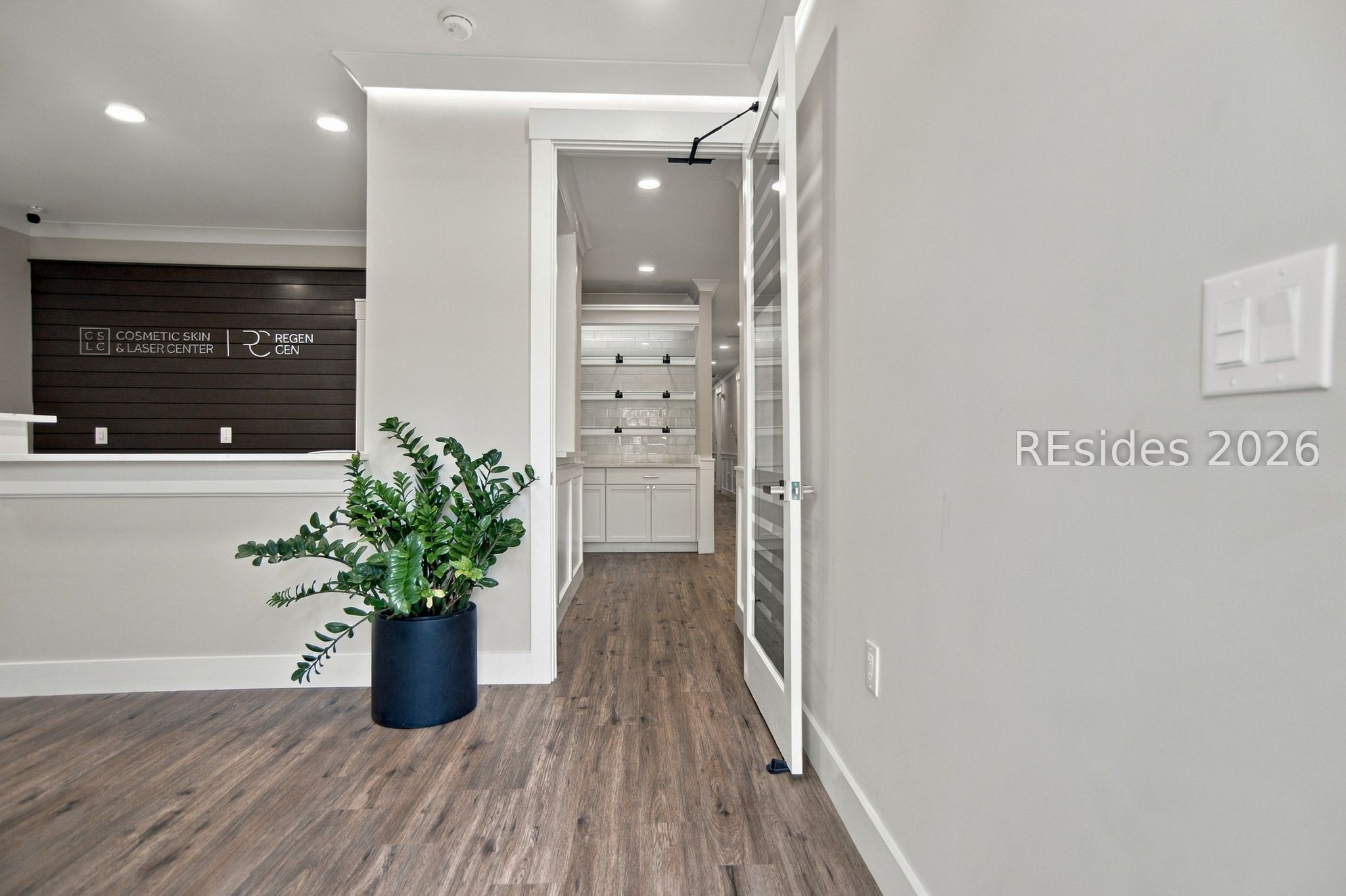Cosmetic skin and laser center reception with dark wood feature wall, potted plant, and open hallway doorway.