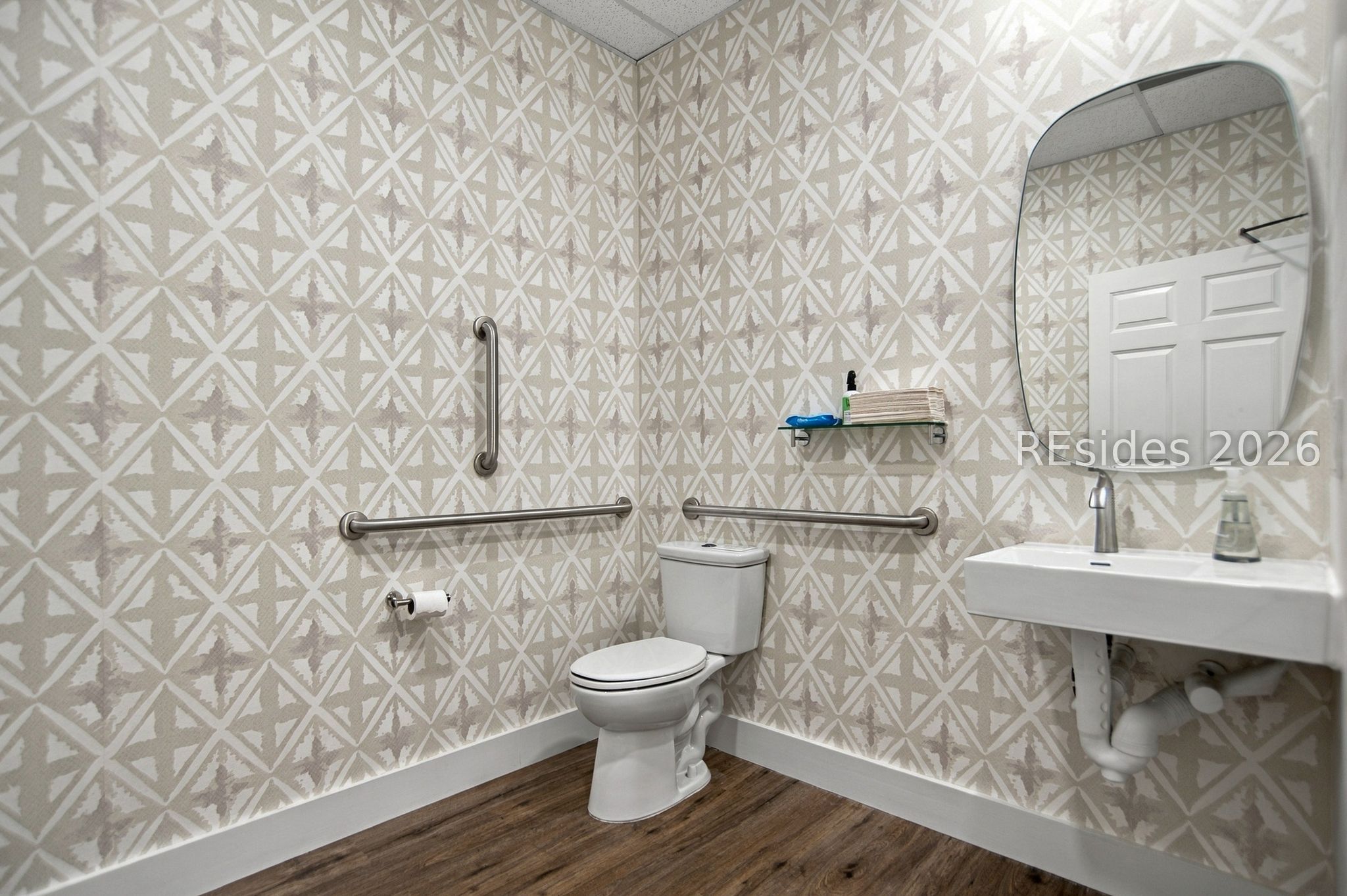 Accessible bathroom with toilet, wall-mounted sink, stainless steel grab bars, and geometric wallpaper.