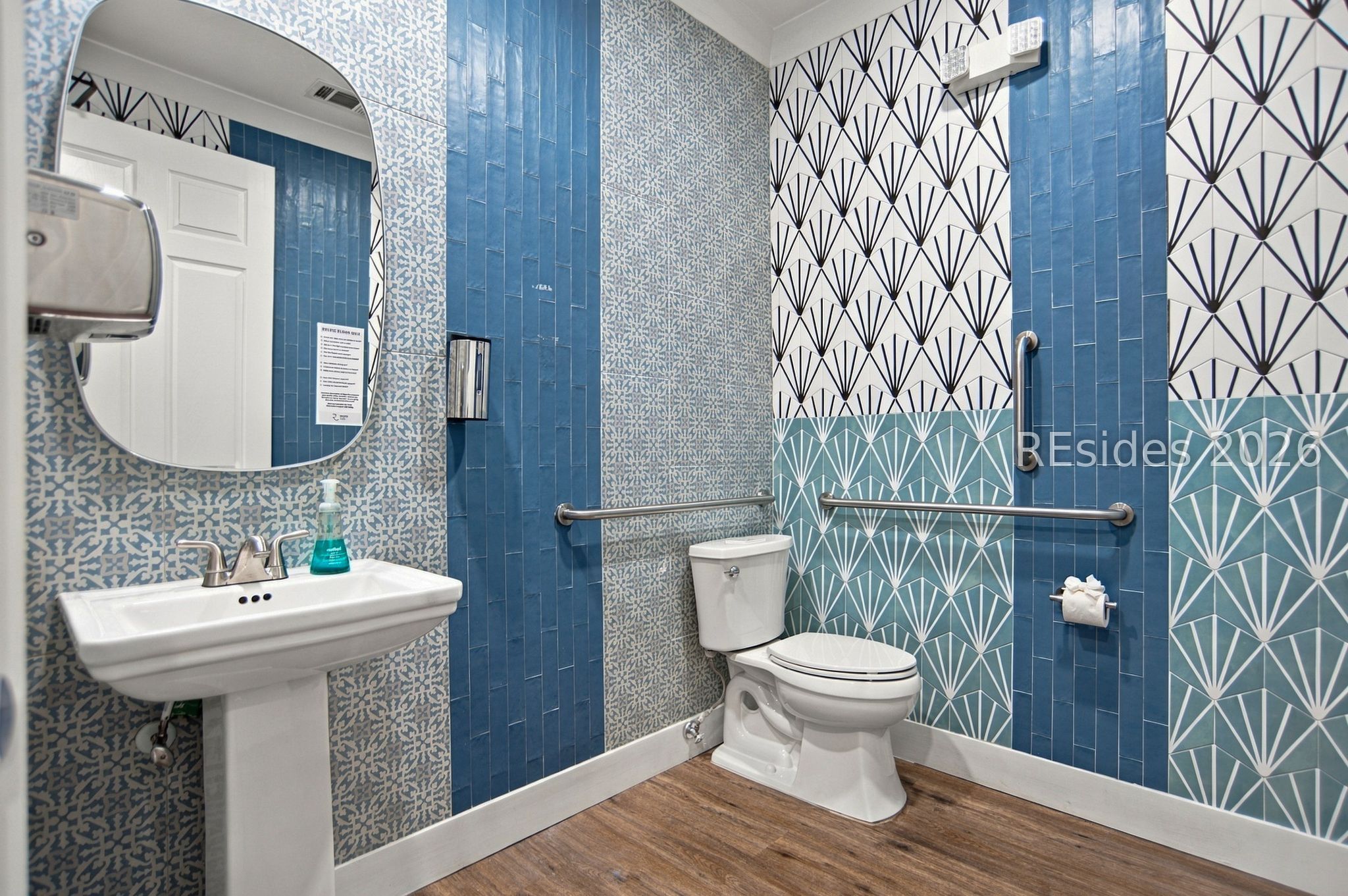 Bathroom with blue geometric tile, a pedestal sink, toilet, and stainless steel grab bars.