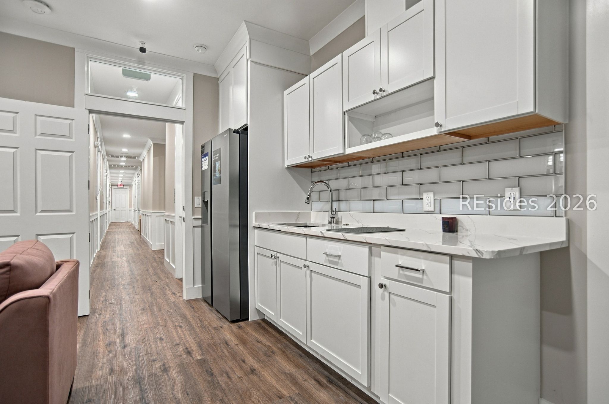 Modern kitchen with white cabinets, stainless steel refrigerator, gray tile backsplash, and wood-look flooring.