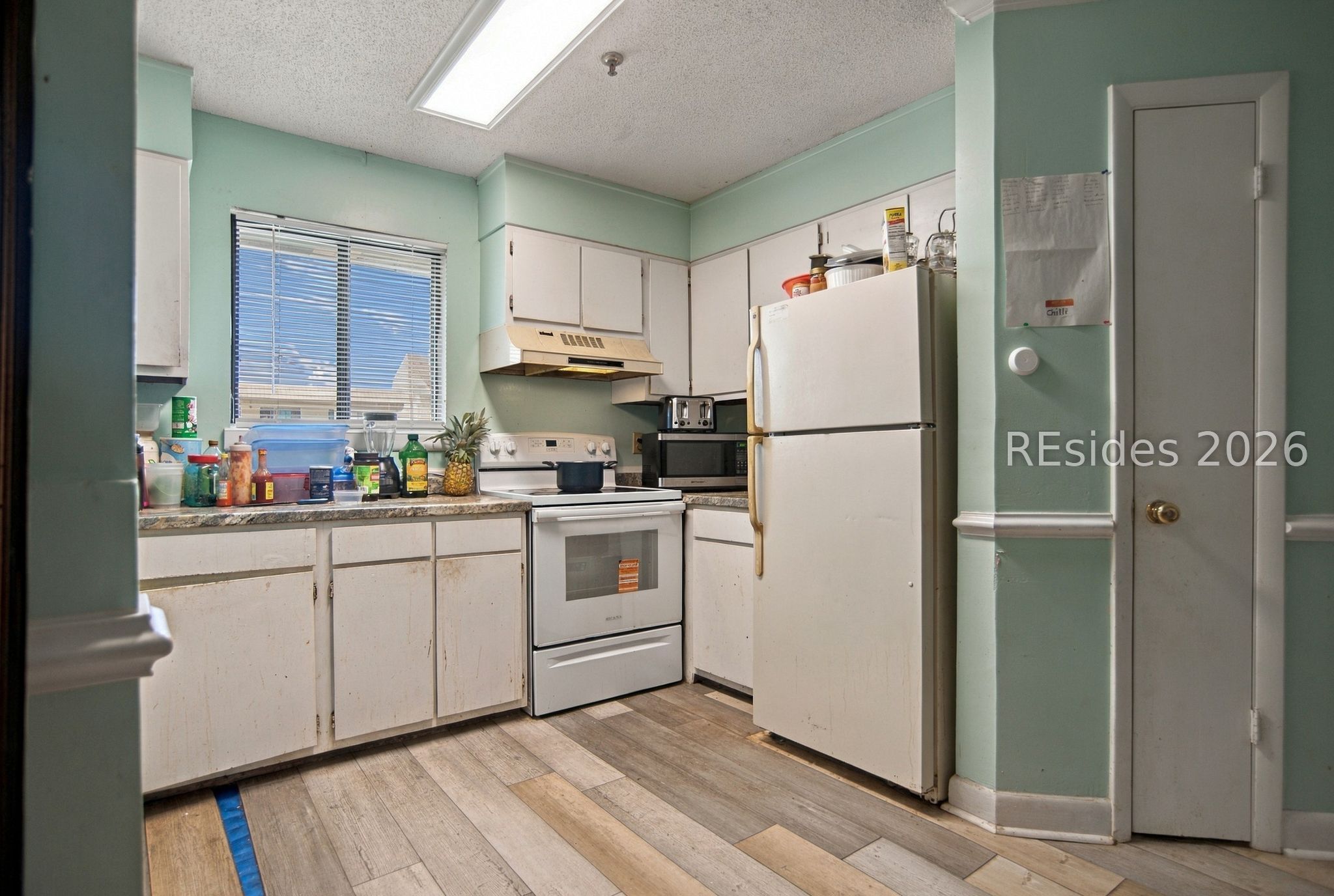Kitchen with white cabinets and appliances, mint-green walls, and wood-look flooring.
