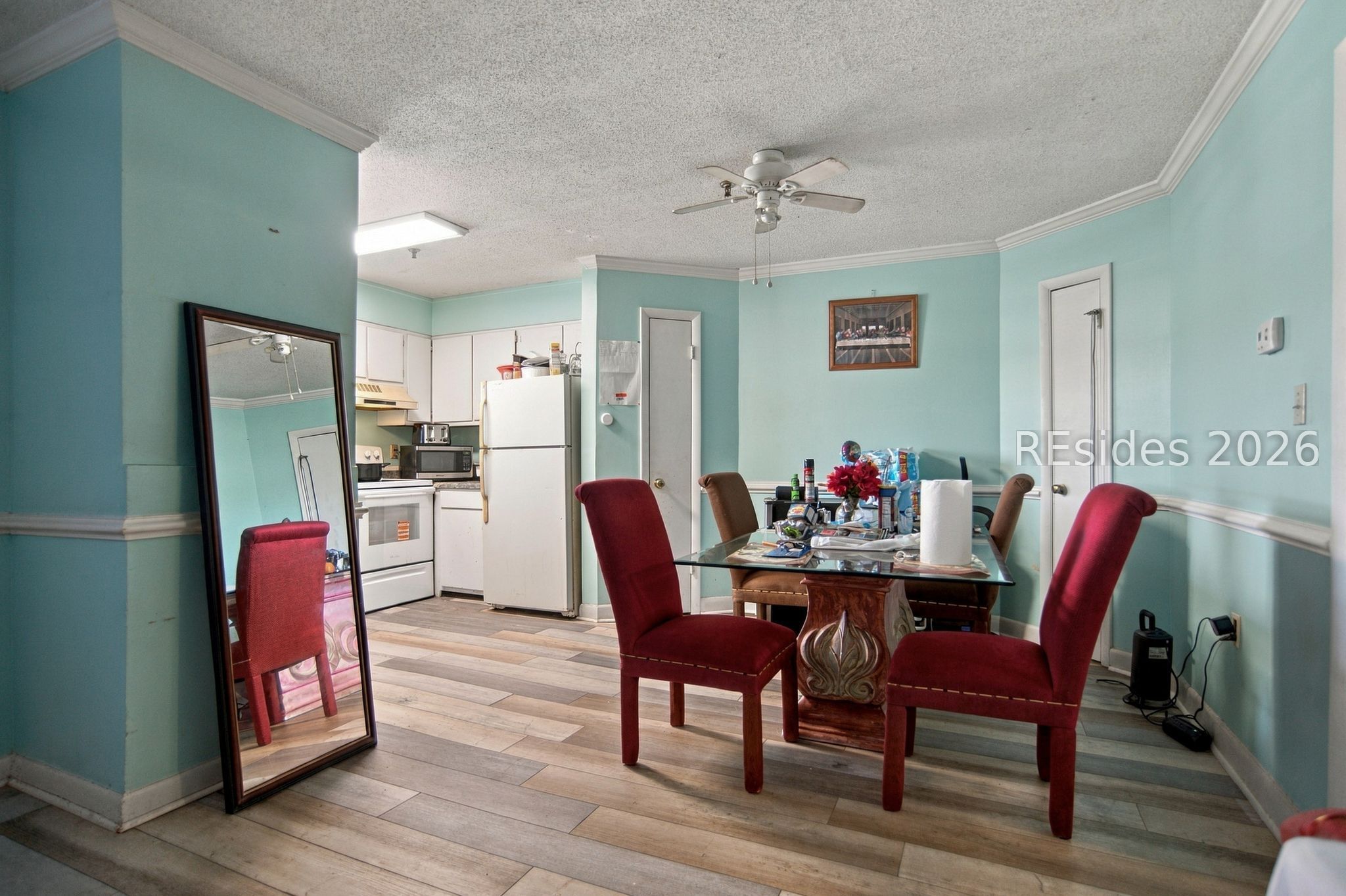 Dining area with red upholstered chairs, a glass-top table, and an adjoining compact kitchen.