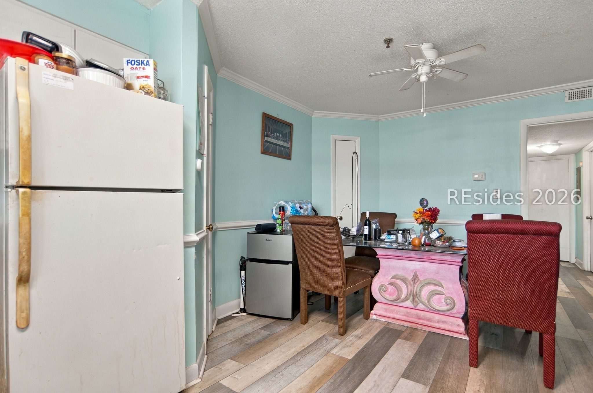 Dining area with a pink pedestal table, red chairs, and a refrigerator against aqua walls.