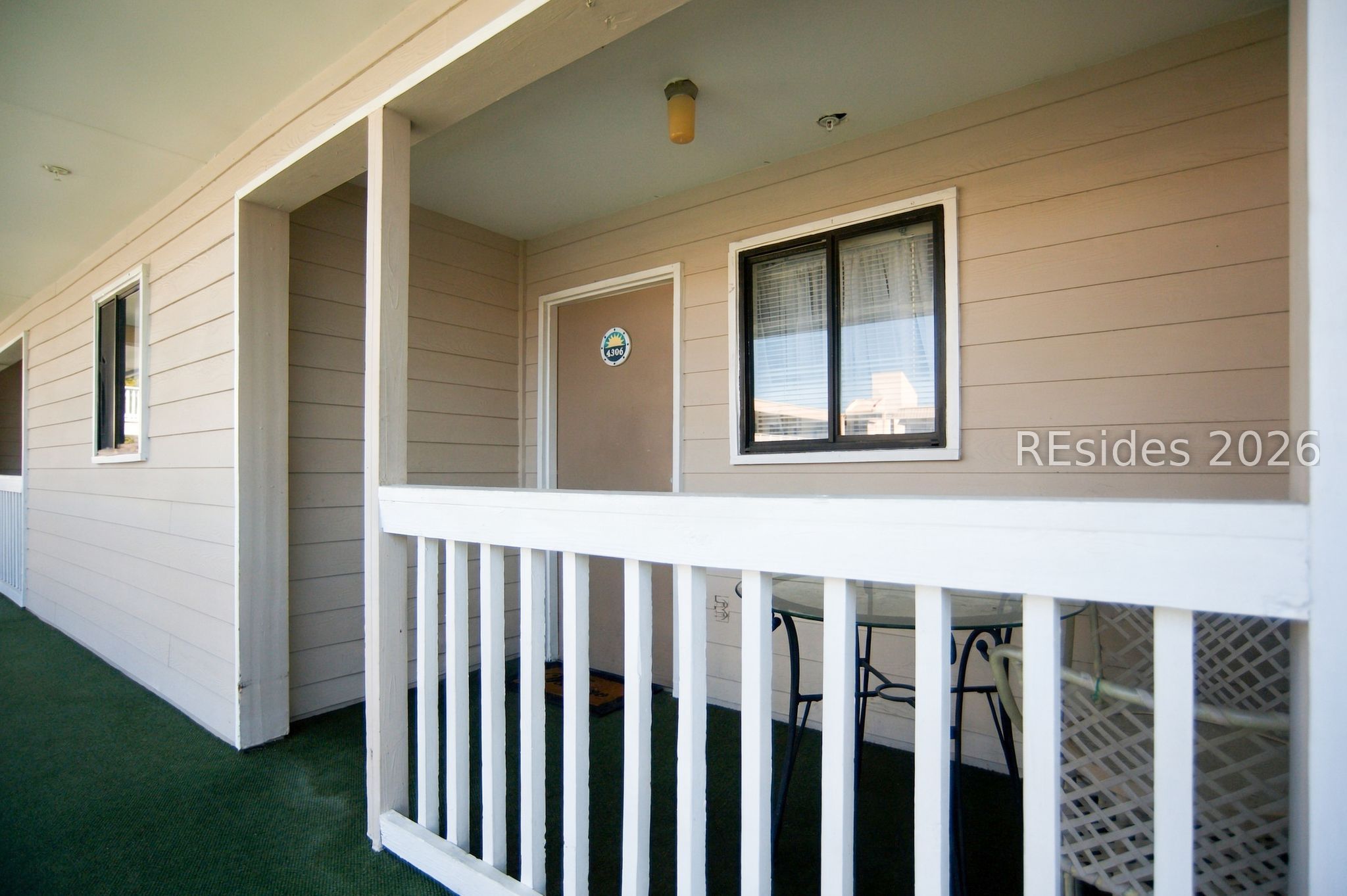 Condo entry balcony with white railing, beige siding, and patio furniture.