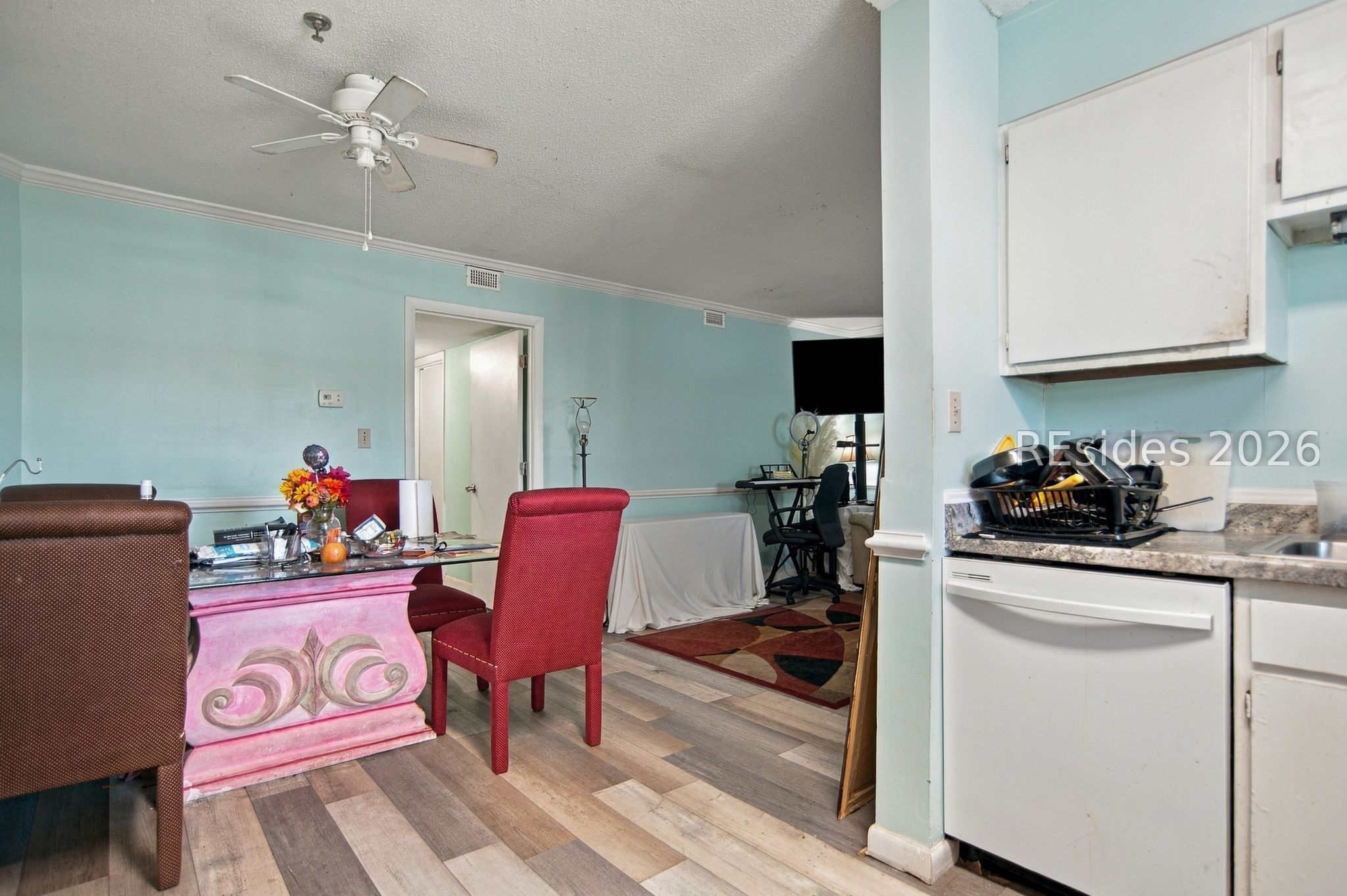 Dining area with a carved pink table and red chairs beside a compact kitchen.