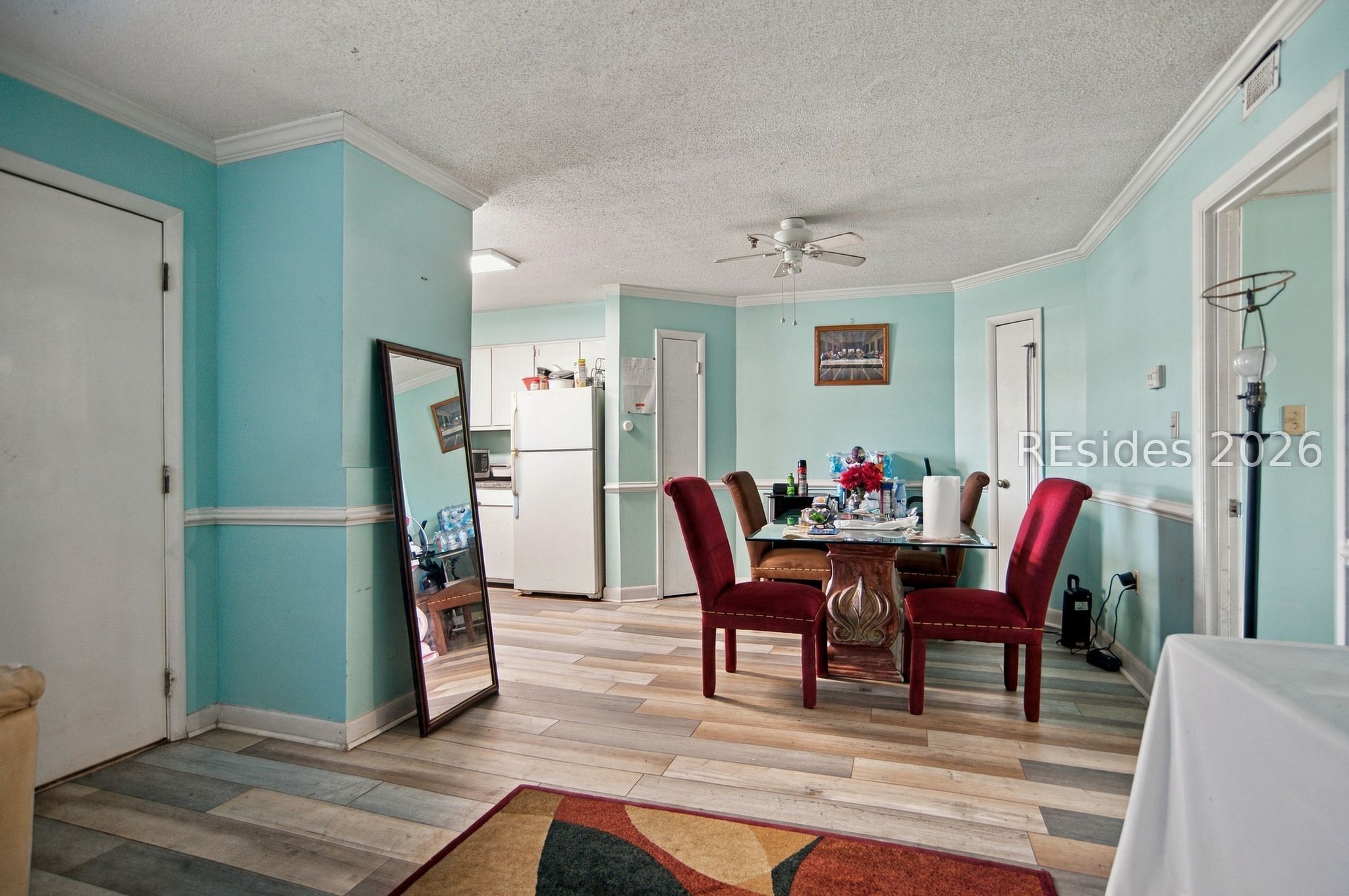 Dining area with a glass-top table, red chairs, turquoise walls, and adjoining kitchen.