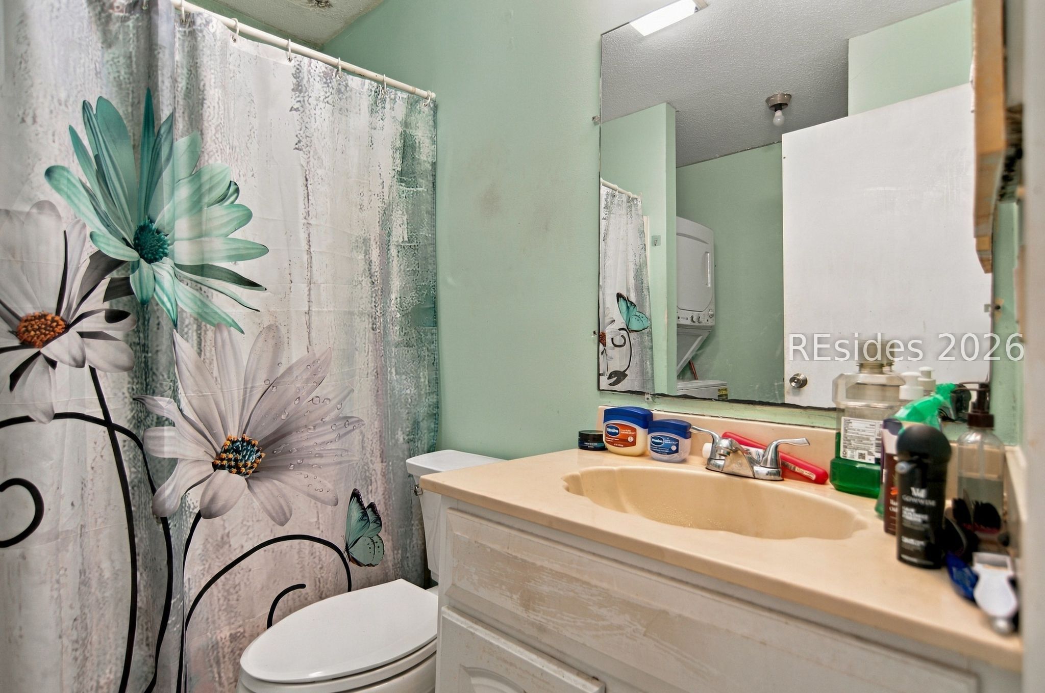 Bathroom with a beige vanity, large mirror, toilet, and bold floral shower curtain.