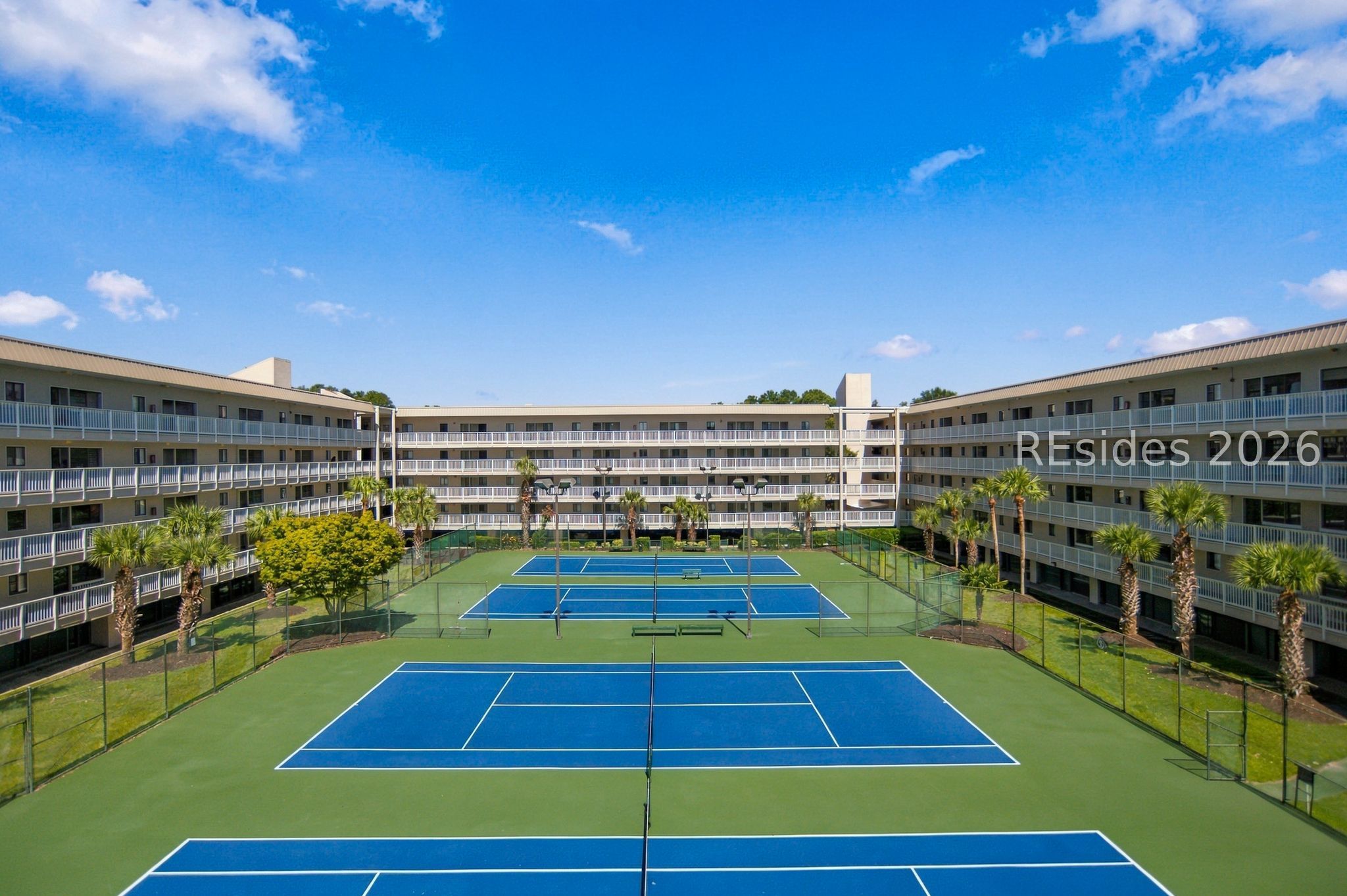 Condominium complex surrounding blue tennis courts, with palm trees and balconies.