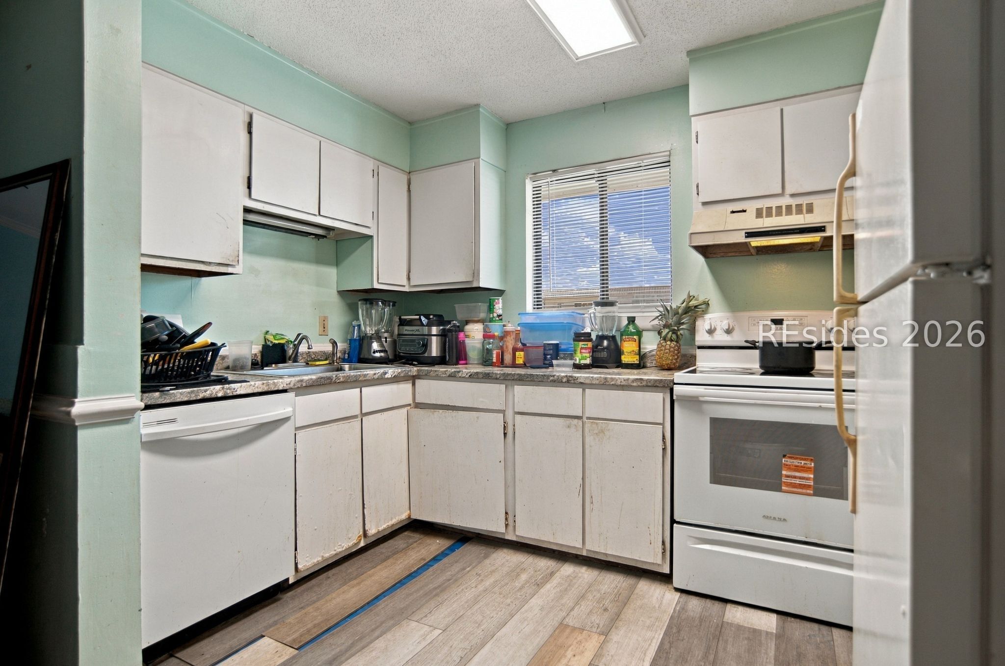 Kitchen with worn white cabinets, mint-green walls, and crowded countertops.