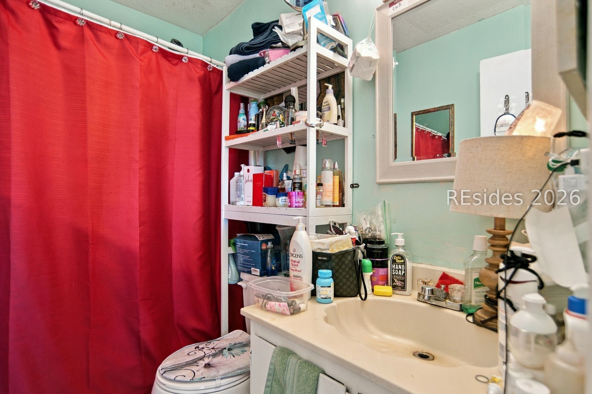 Bathroom with a white vanity, red shower curtain, and open shelves crowded with toiletries.