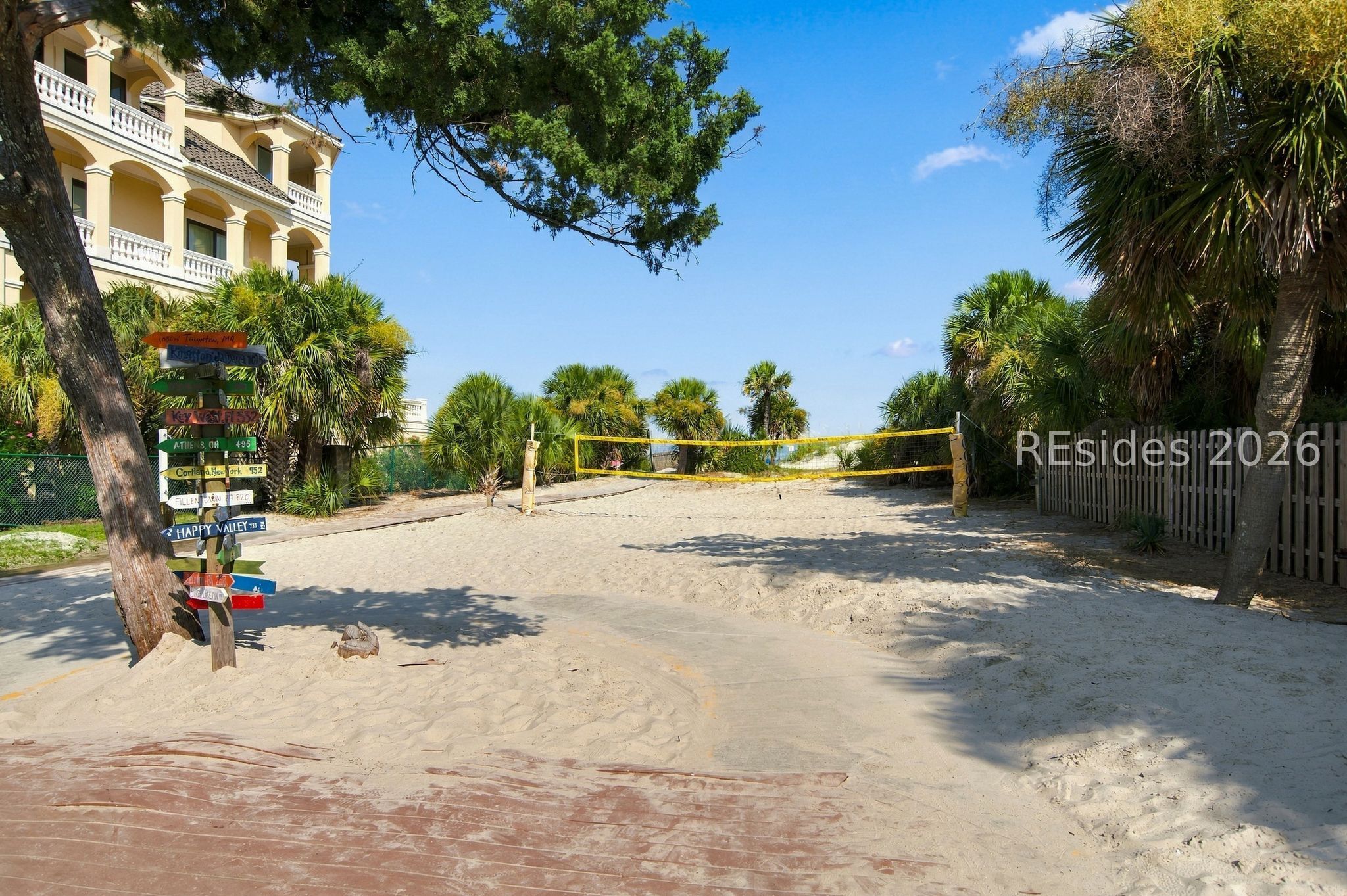 Sandy volleyball court with a yellow net and palm trees beside a condominium.