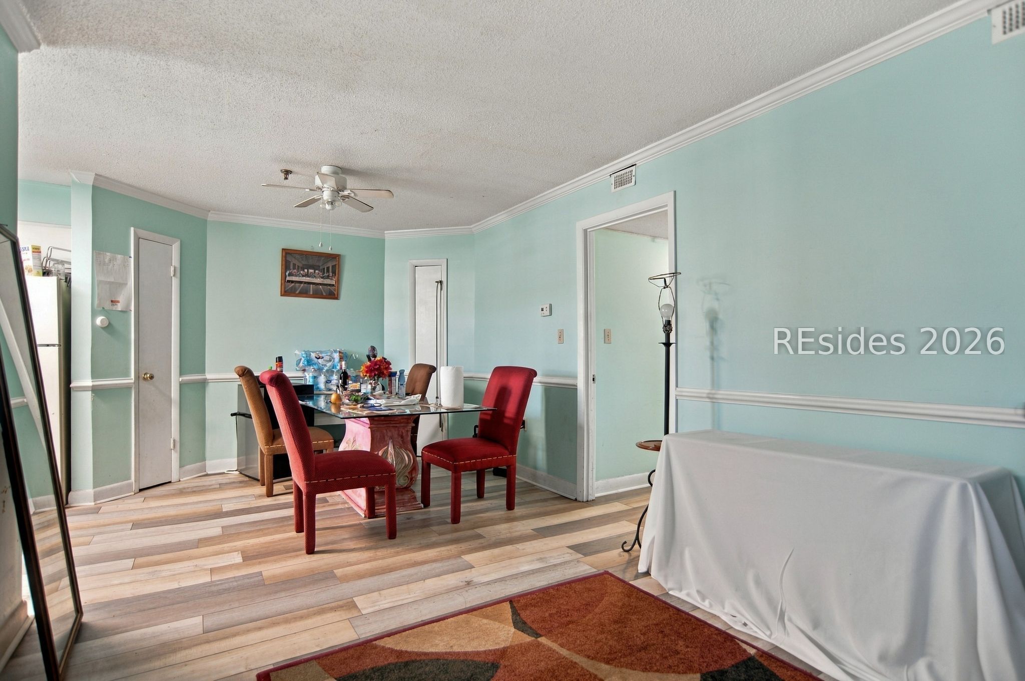 Dining room with pale aqua walls, a glass table, red chairs, and wood-look flooring.