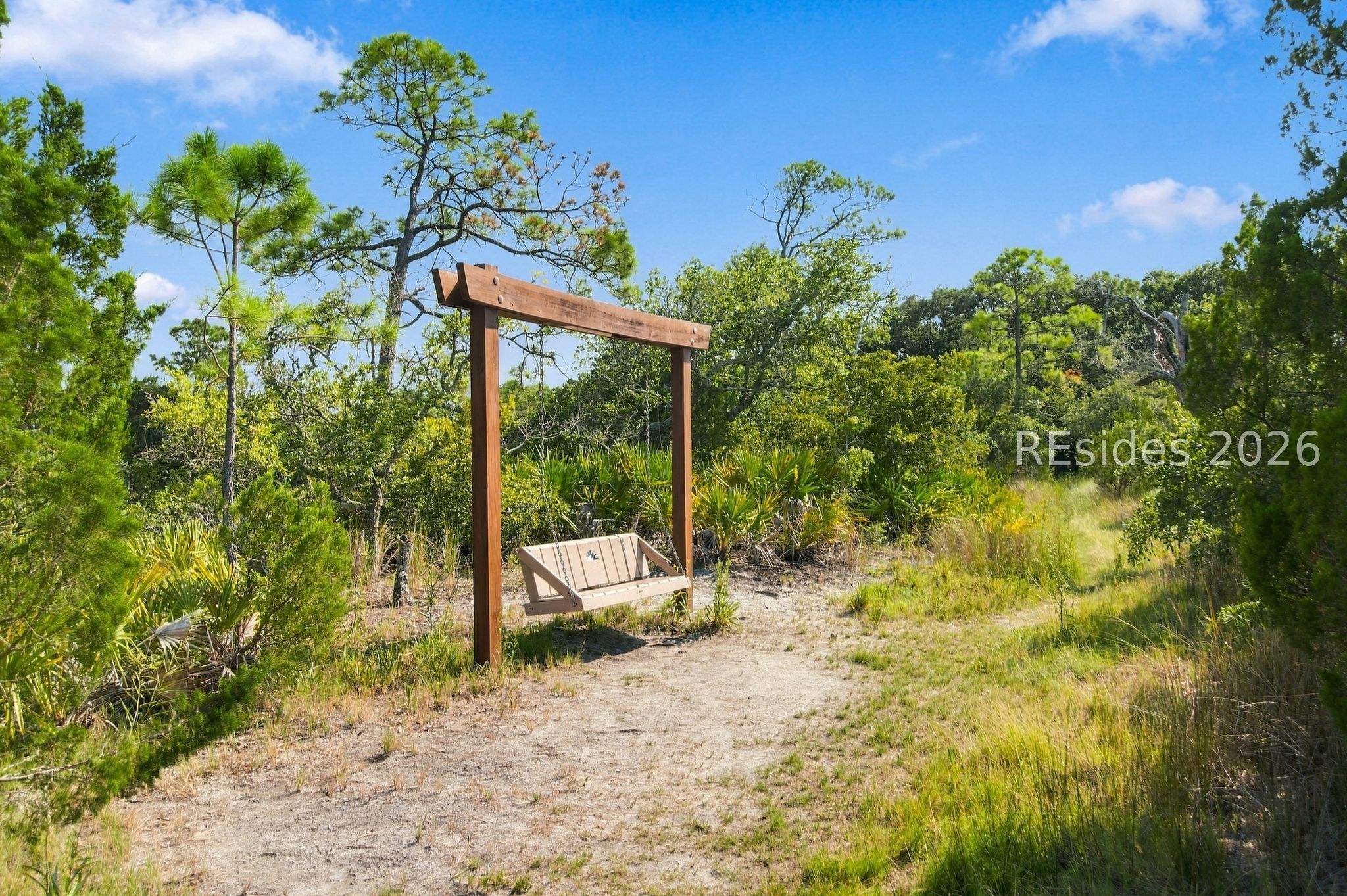 Wooden garden swing beside a sandy path in lush coastal landscaping.