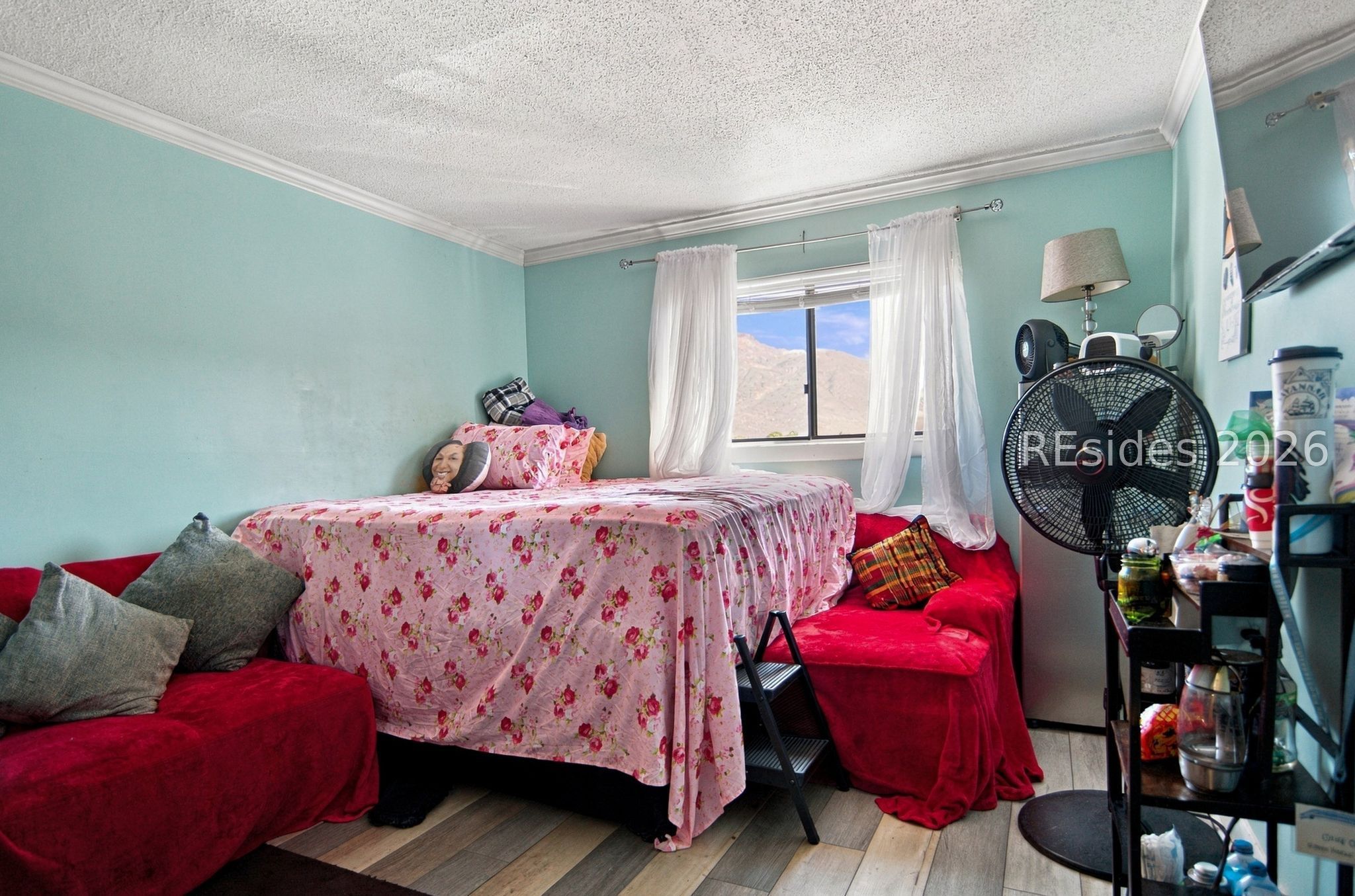 Bedroom with a floral-covered bed, red seating, and a mountain view through the window.