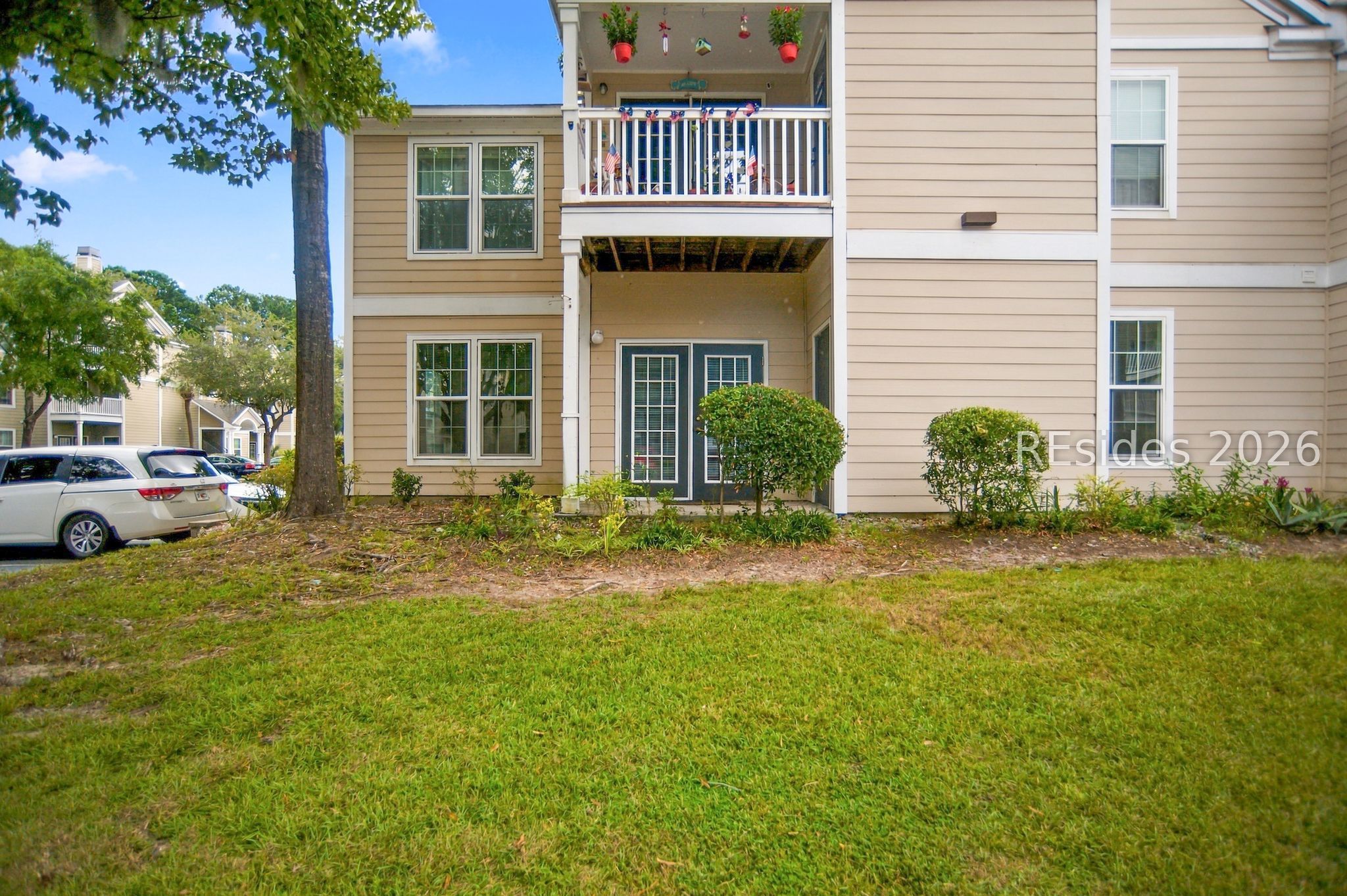 Beige condominium exterior with a covered entry and balcony decorated with hanging plants and flags.