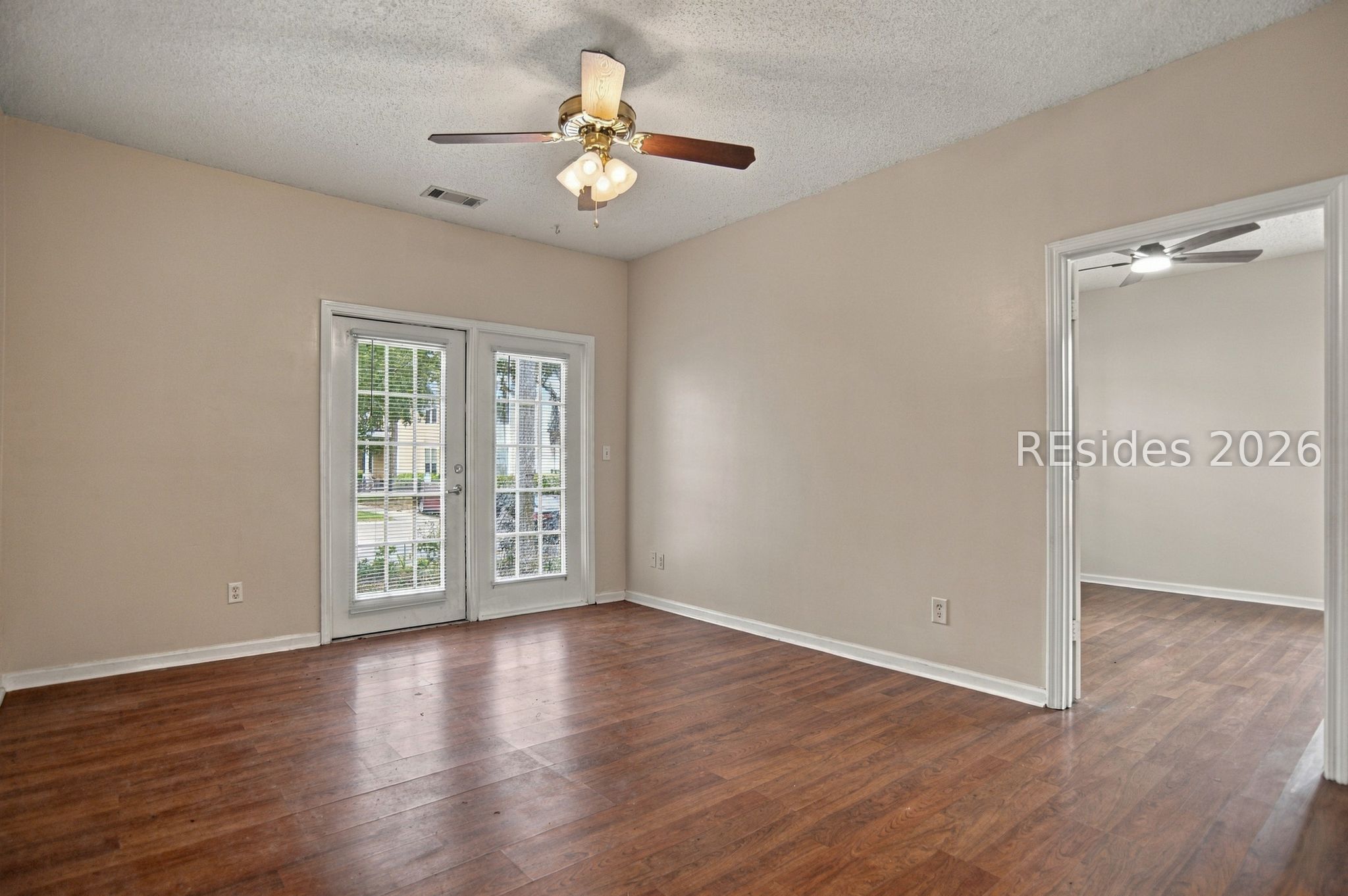 Empty room with dark wood flooring, a glass-paned exterior door, and an adjoining room through an open doorway.
