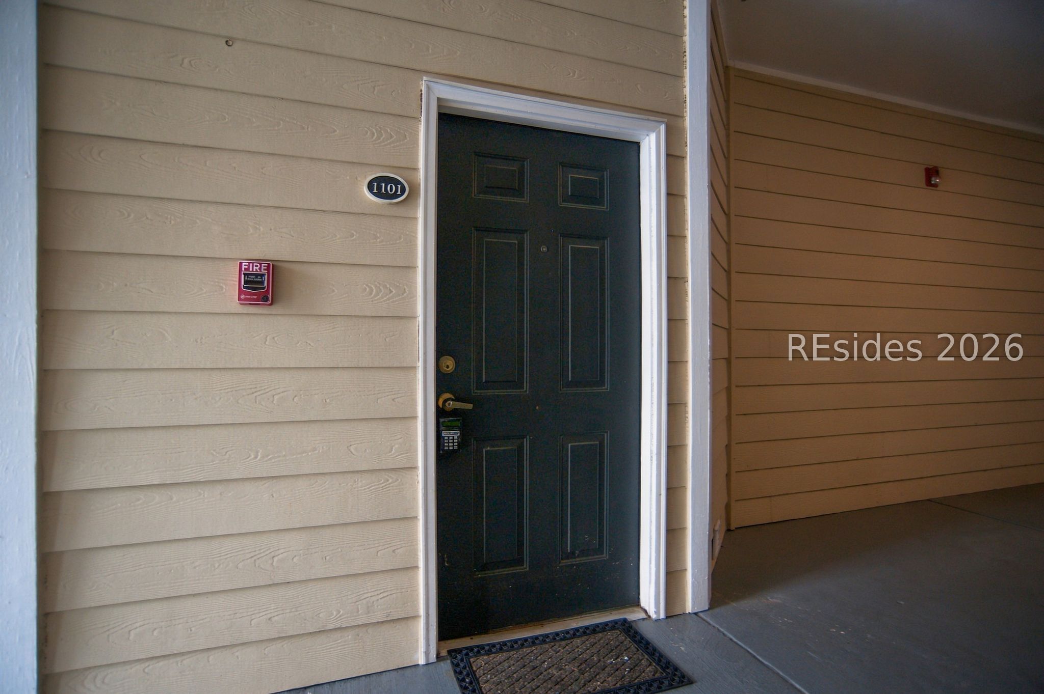 Unit 1101 entrance with a dark paneled door, keypad lock, and beige siding.
