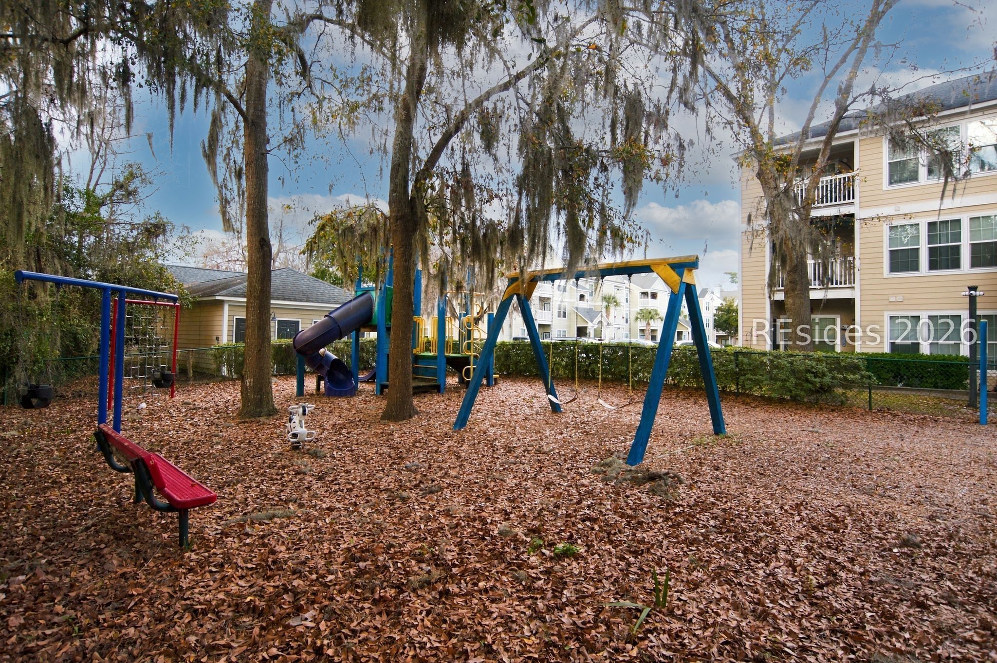 Residential playground with swings and a slide beneath Spanish moss-draped trees.