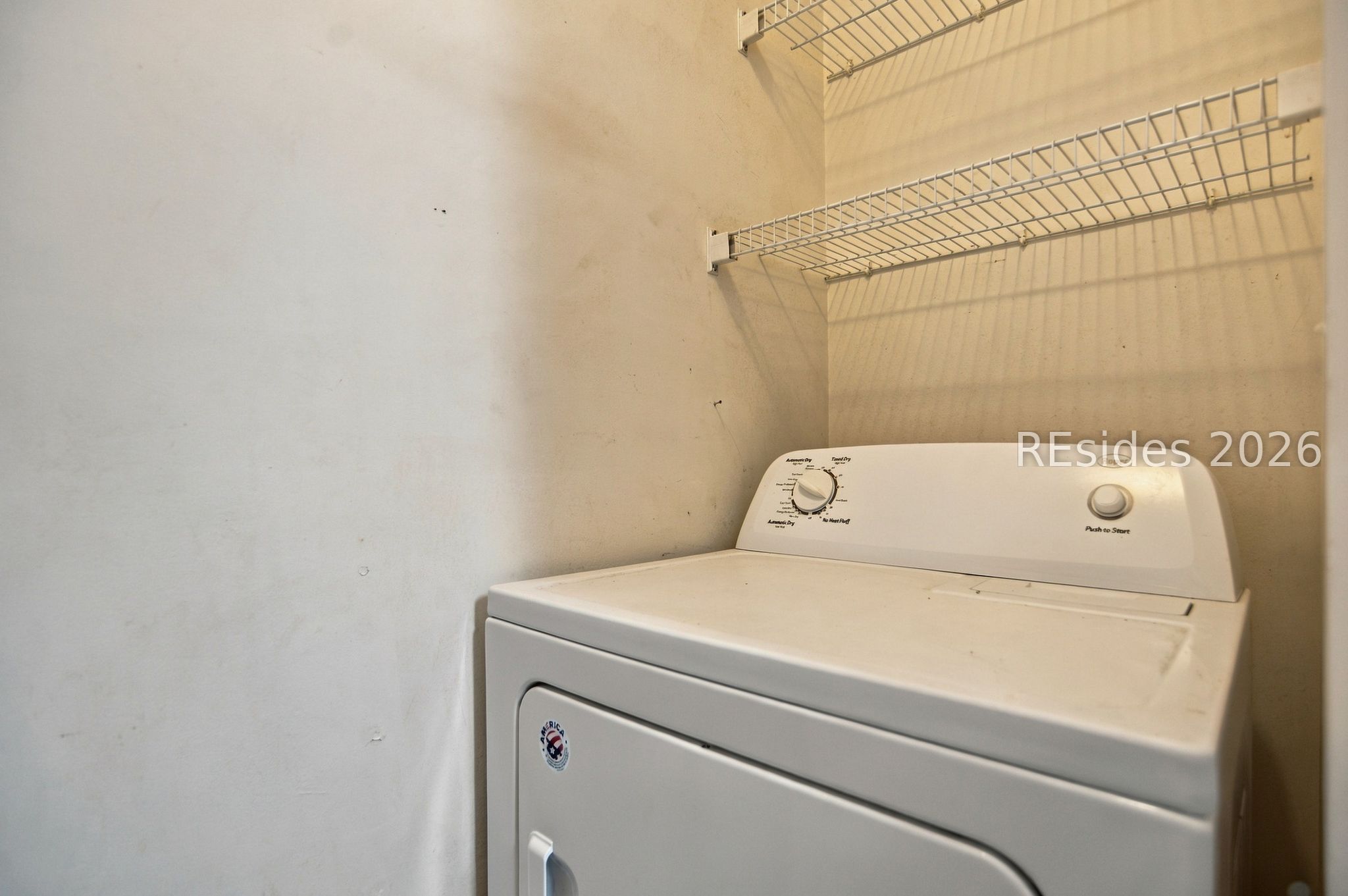 Laundry area with a white dryer beneath wall-mounted wire shelves.