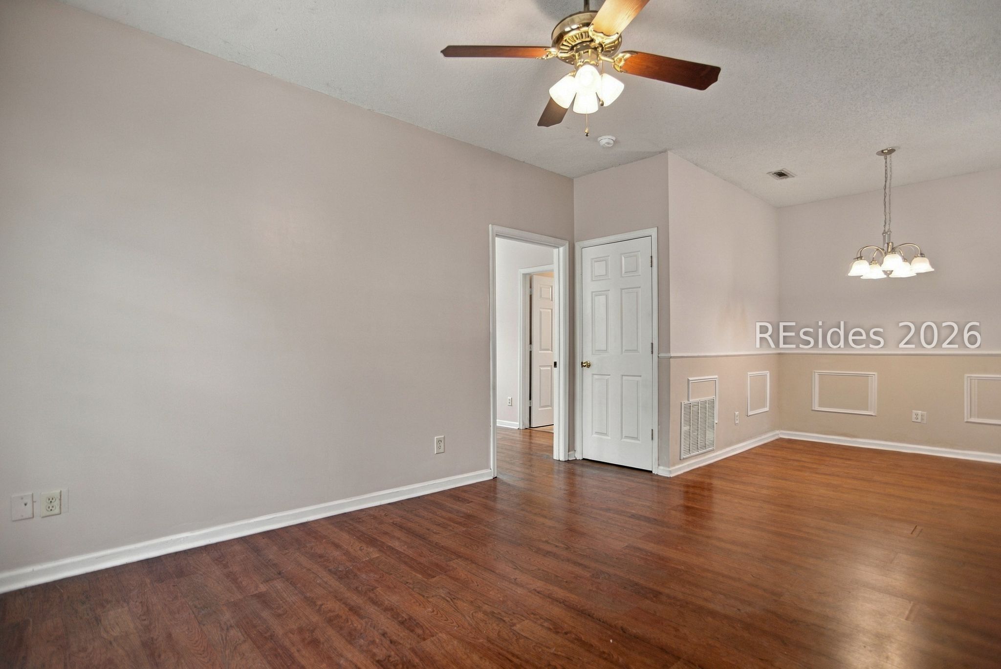 Empty dining room with hardwood floors, decorative wainscoting, a ceiling fan, and chandelier.