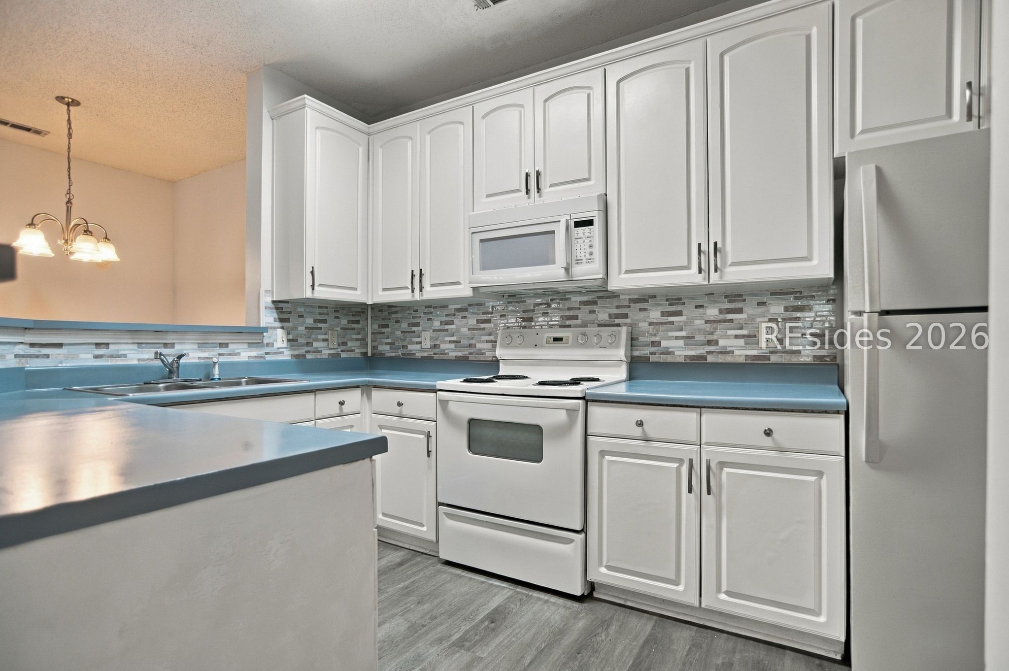 Kitchen with white cabinets, blue countertops, mosaic tile backsplash, and white appliances.