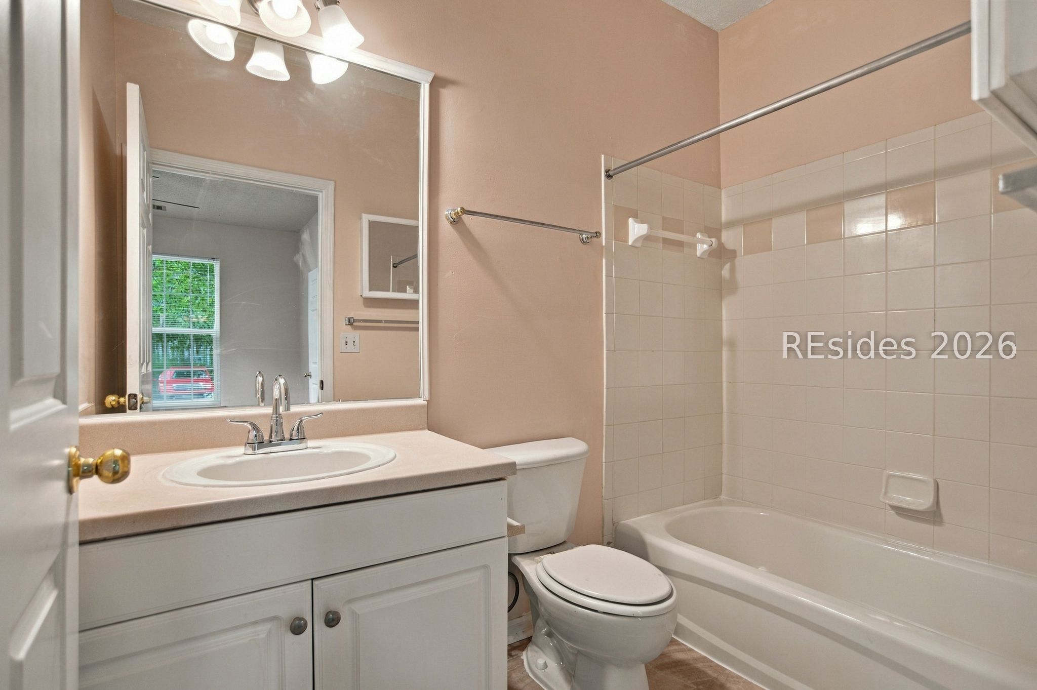Bathroom with white vanity, toilet, and bathtub beneath a beige tiled surround.
