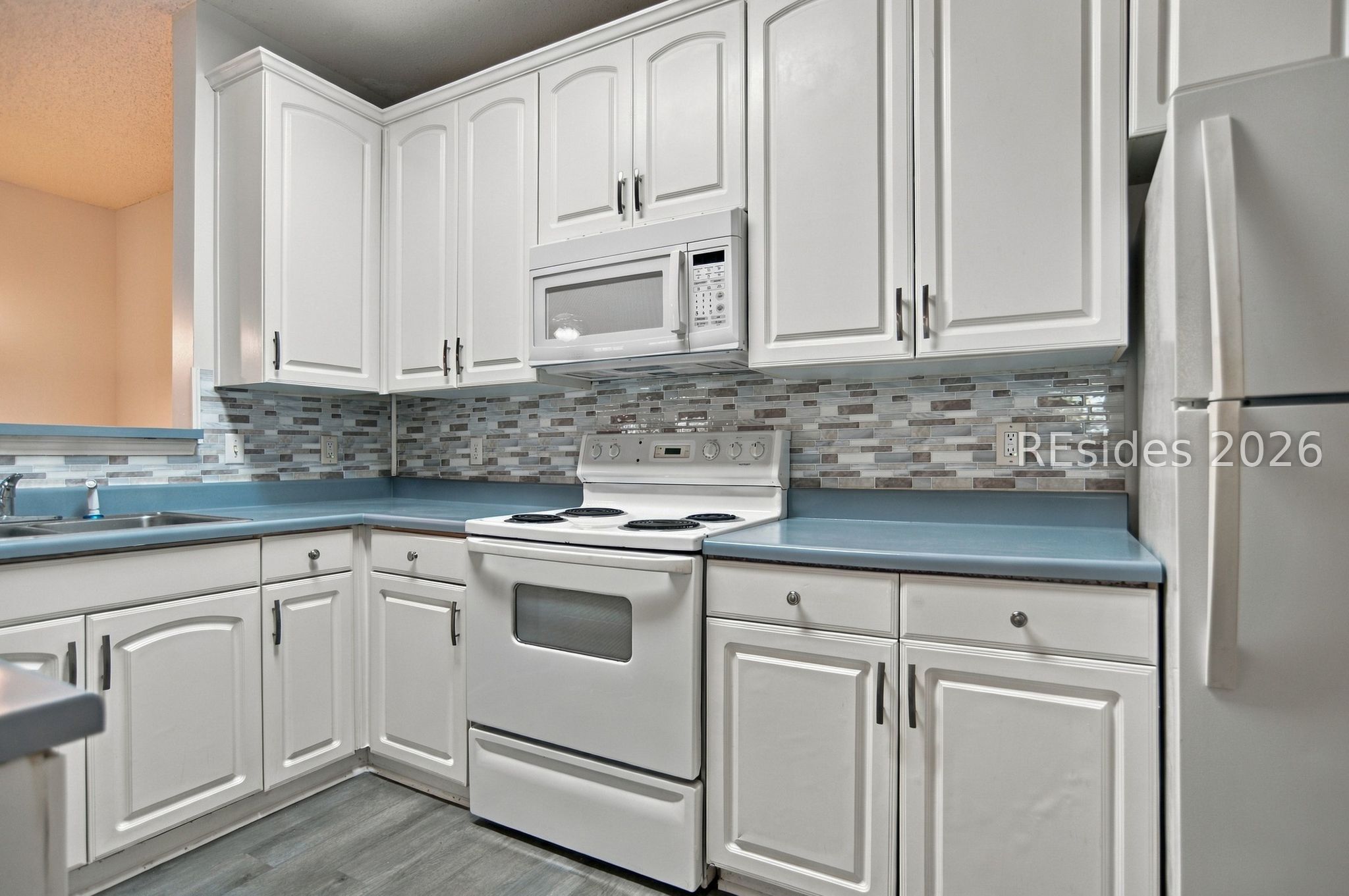 Kitchen with white cabinets, blue countertops, mosaic backsplash, and white electric range and refrigerator.