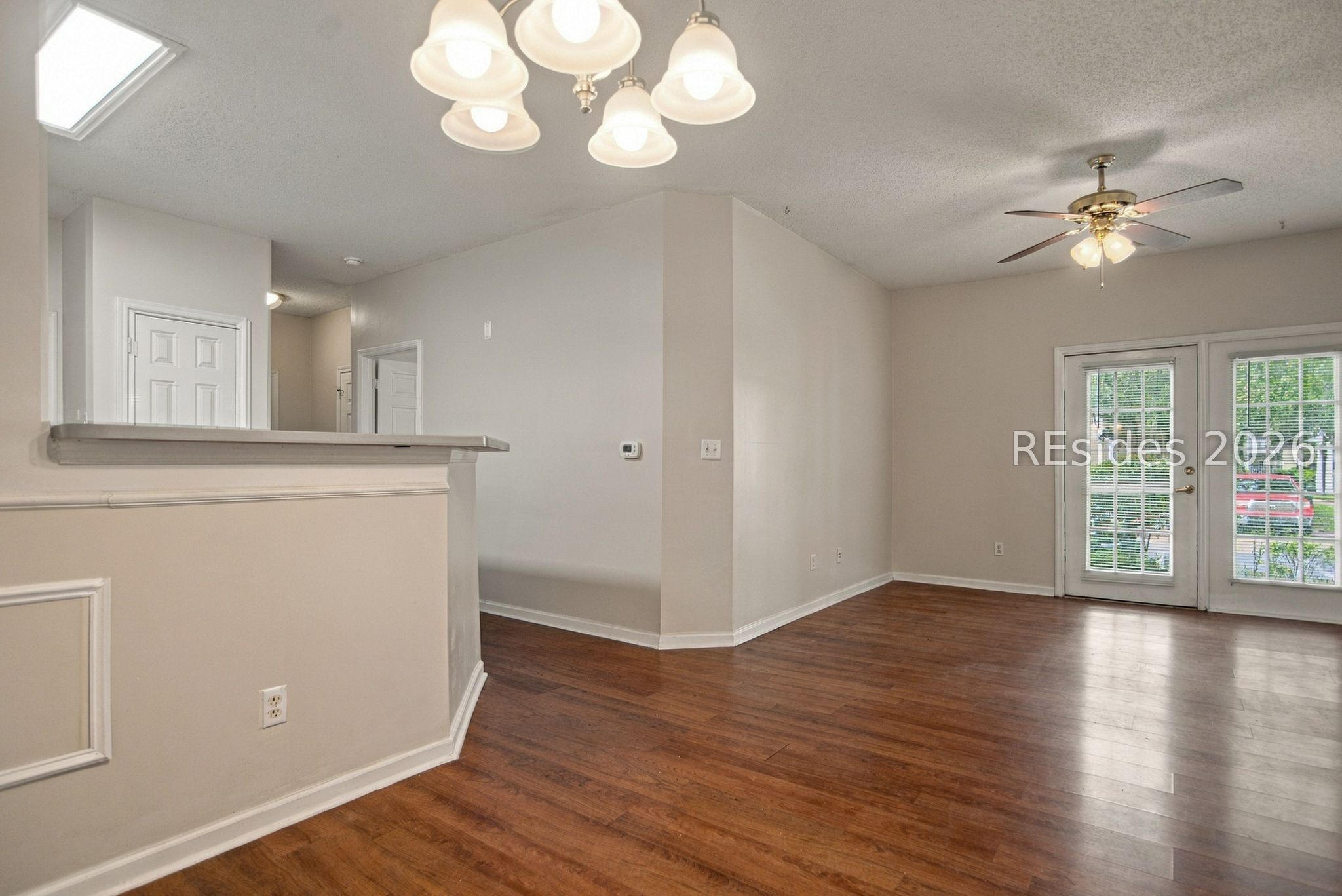 Empty dining and living area with dark wood floors and French doors.