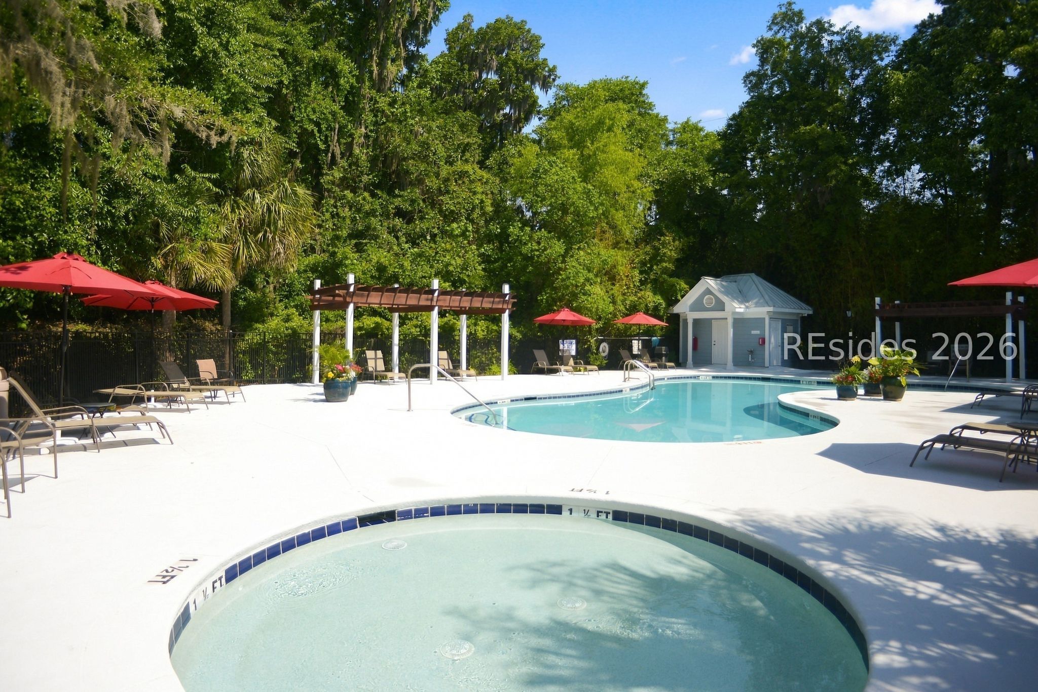 Outdoor swimming pool and shallow wading pool with red umbrellas and a wooded backdrop.