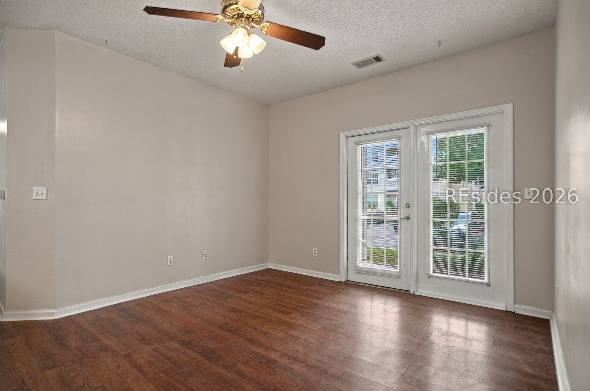 Empty room with dark wood flooring, a ceiling fan, and a glass door beside a window.