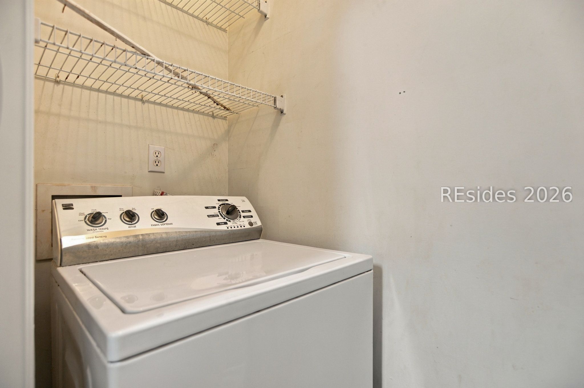 Top-loading washer beneath wire shelving in a laundry closet.