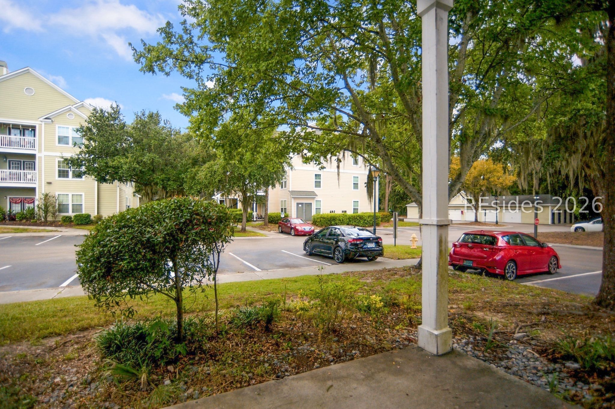 Condominium community with pale yellow buildings, mature trees, and a parking lot.