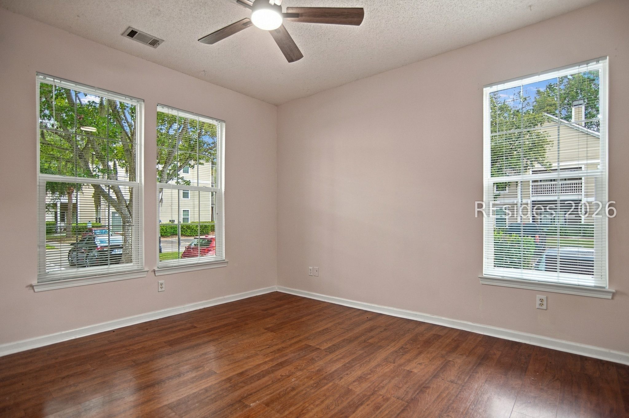 Vacant room with hardwood floors, three windowed walls, and a ceiling fan.